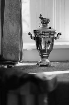 A nostalgic black and white photo of a polished metal samovar by a window with shadows.