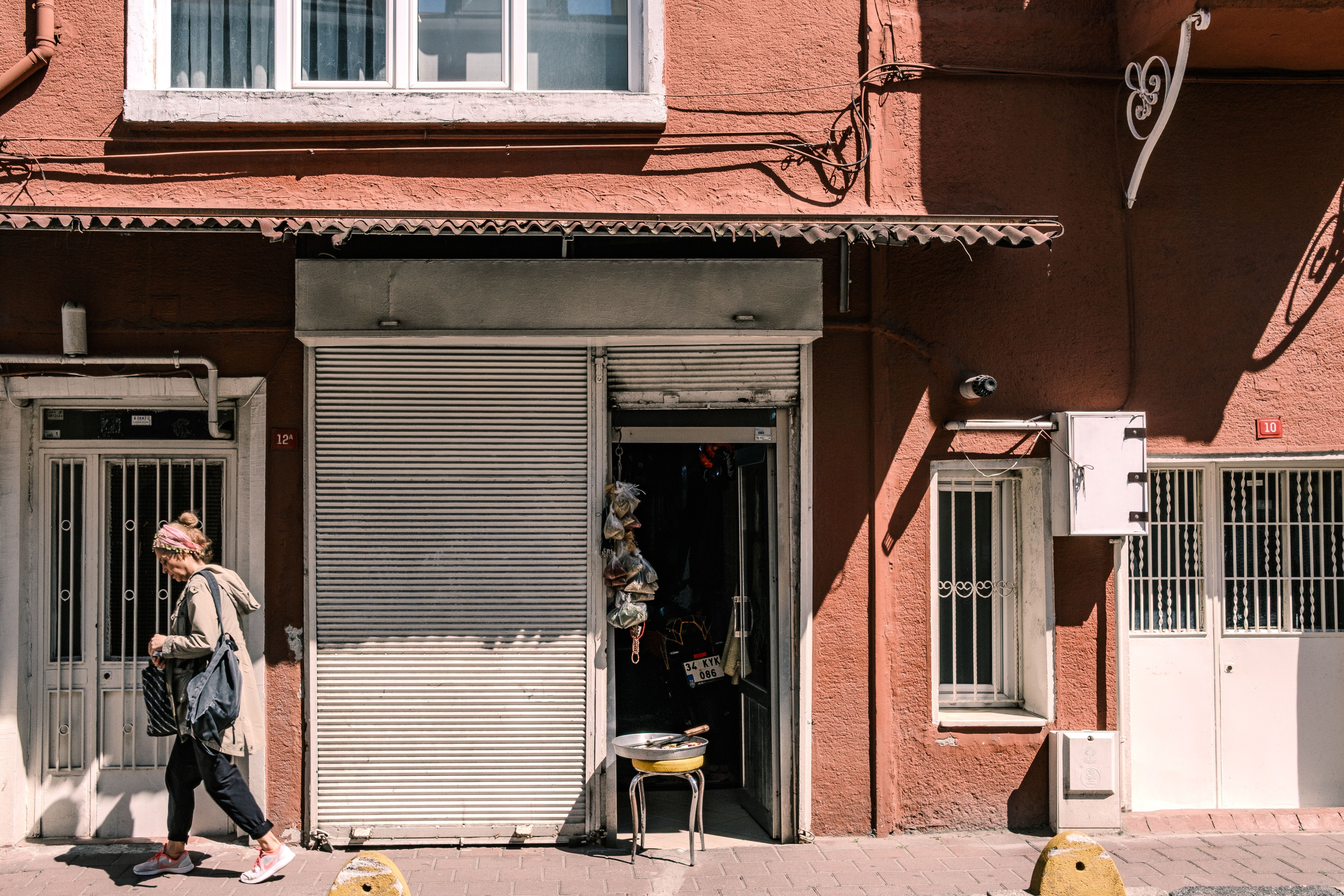 A pedestrian walks past a closed urban storefront under bright daylight, capturing street life.