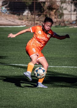 Young female soccer player kicking the ball during training on a grassy field.