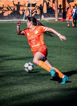 Dynamic shot of a female soccer player in orange uniform dribbling a ball during a match.