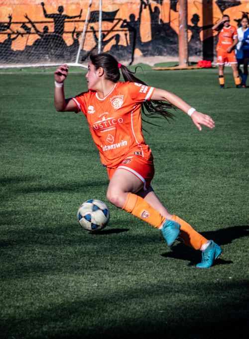 Free Dynamic shot of a female soccer player in orange uniform dribbling a ball during a match. Stock Photo
