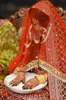 Elegant South Asian bride adorned with henna and colorful veil, holding decorative tray.