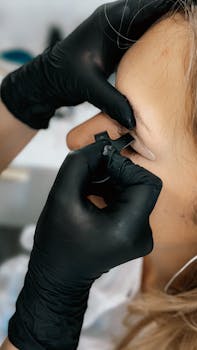 Close-up of a person receiving an eyebrow tattoo by a professional artist wearing gloves.