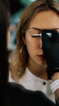 Close-up of a makeup artist applying eyeshadow to a young woman in a studio setting.