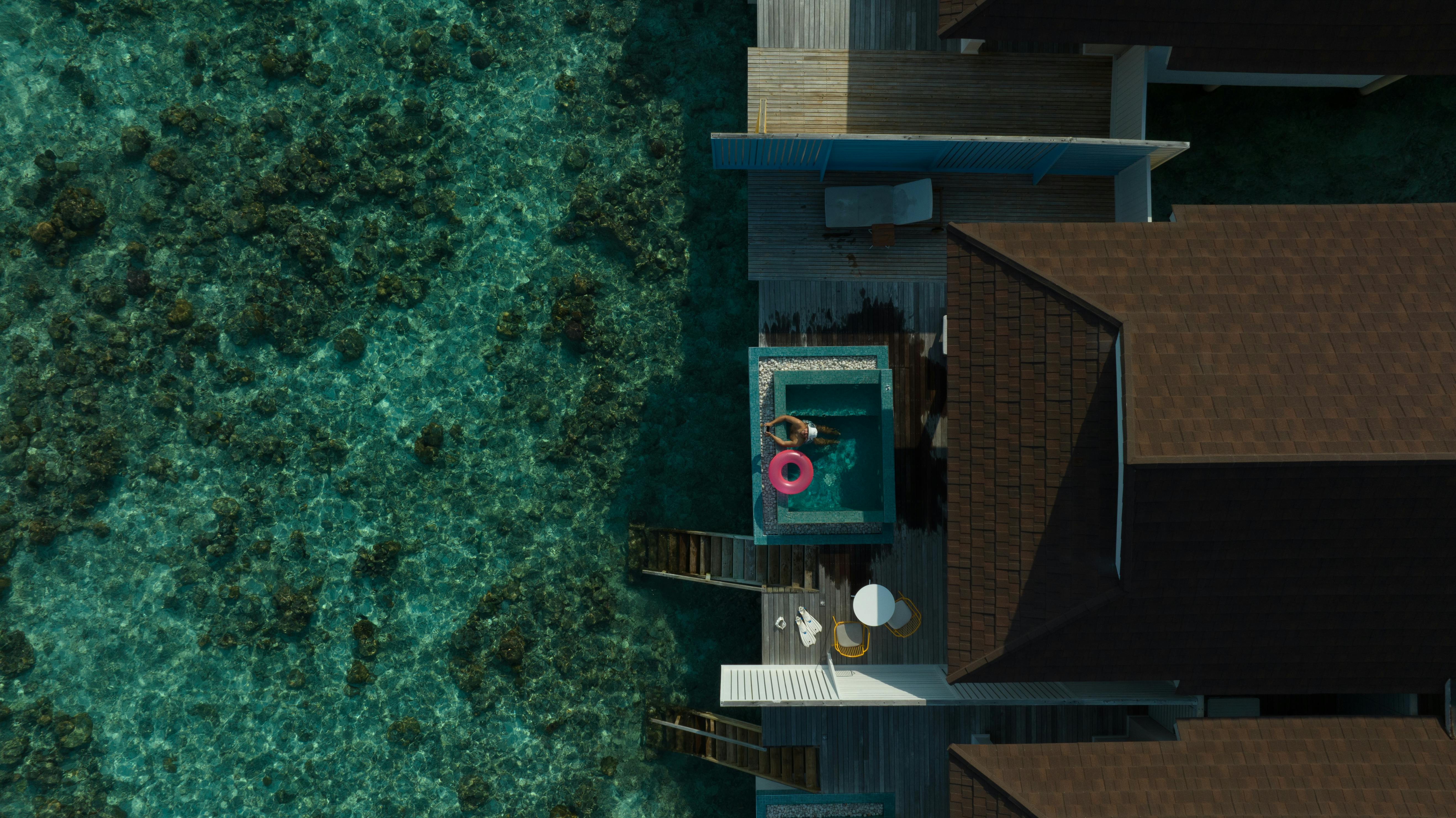 Stunning aerial view of a Maldives overwater villa with clear lagoon, featuring a bright pool float. - Photo by Max Zaharenkov on Pexels