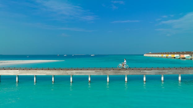 A person rides a bicycle on a pier over clear blue waters in the Maldives. Scenic summer view.