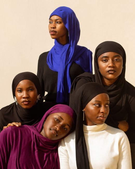 Five women in colorful hijabs and outfits pose confidently outdoors in natural light.