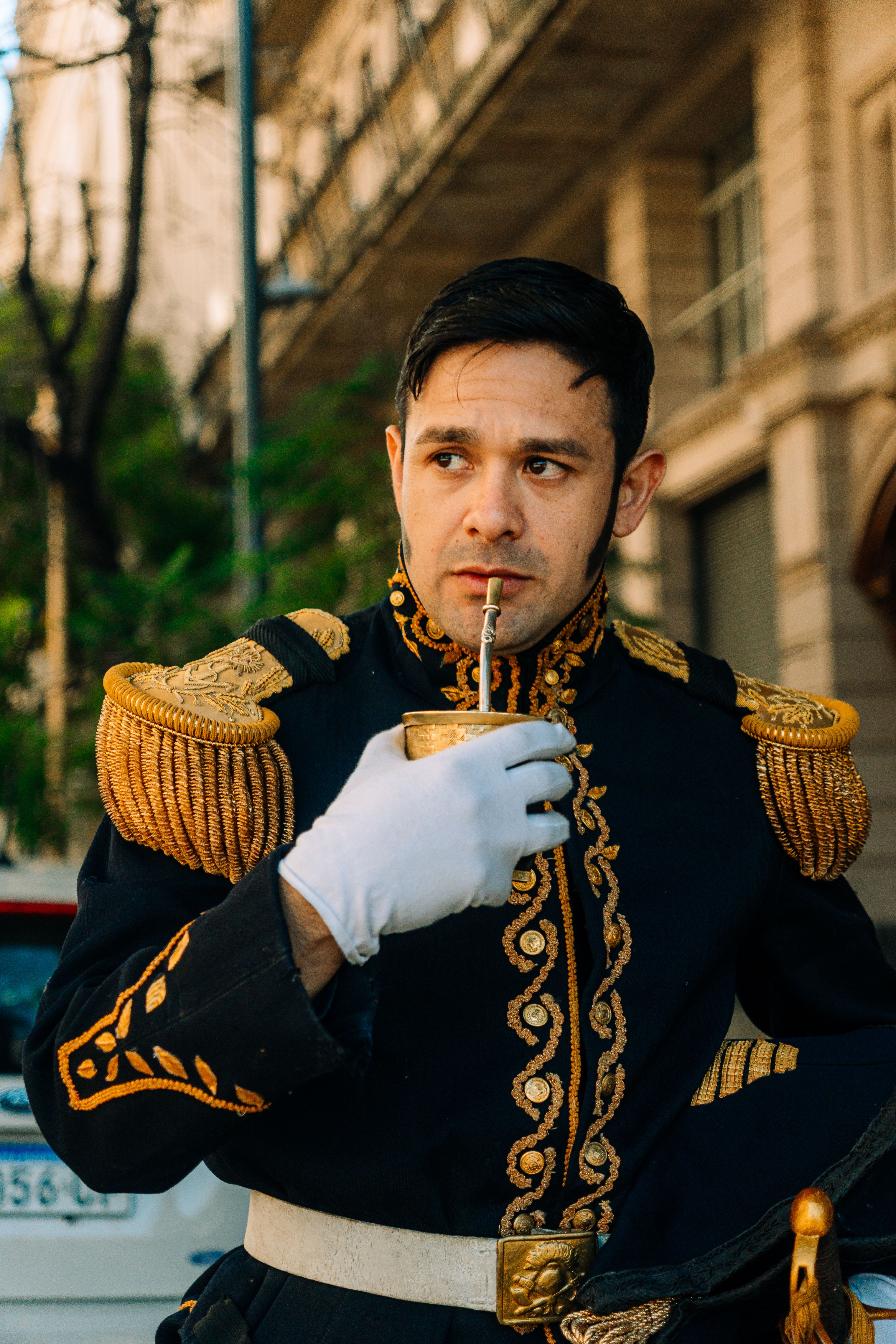 Portrait of a man in traditional Argentine military uniform sipping mate outdoors.