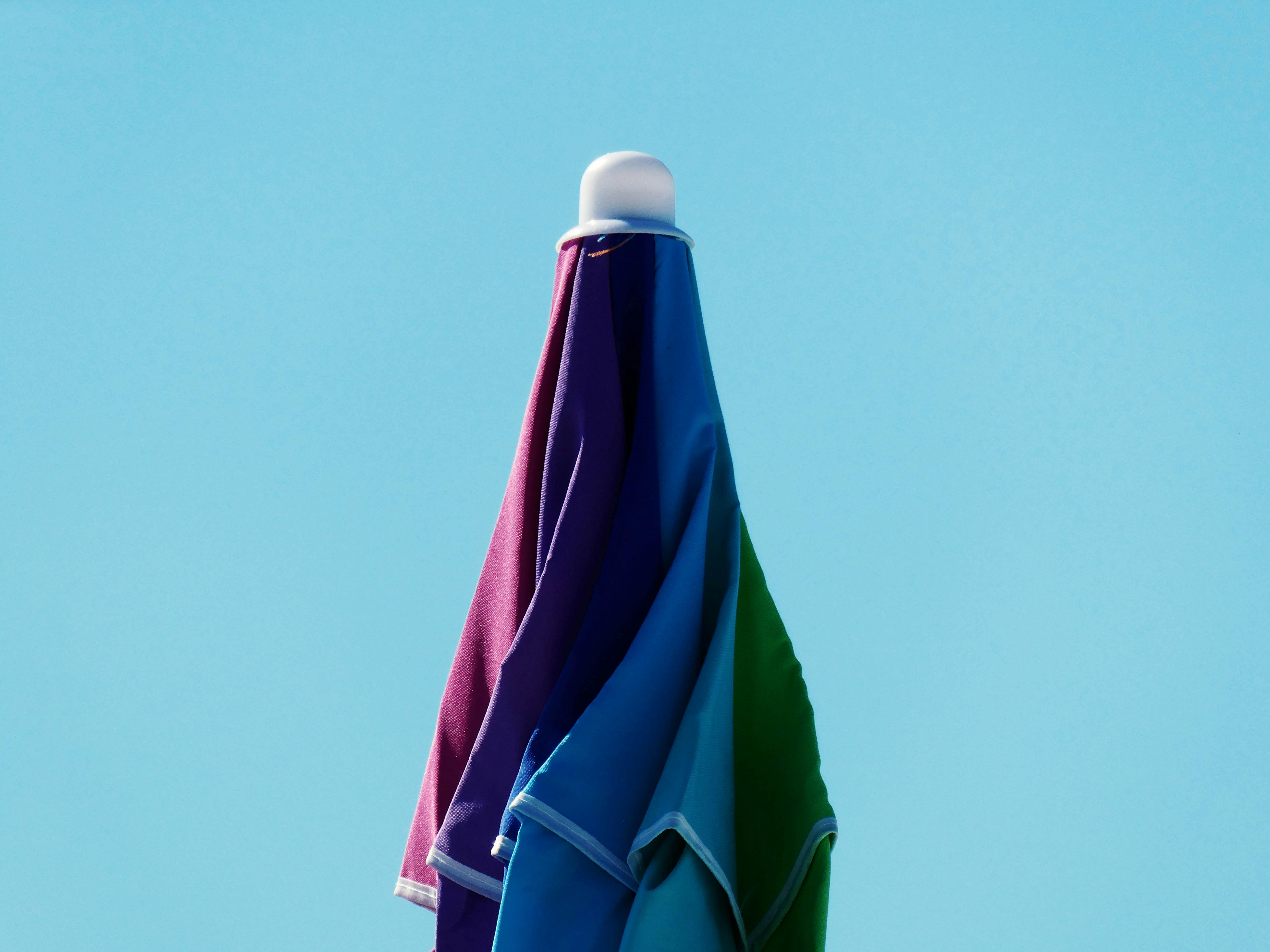 Gratis Una sombrilla de playa vibrante que muestra múltiples colores con un cielo azul claro como fondo. Foto de stock