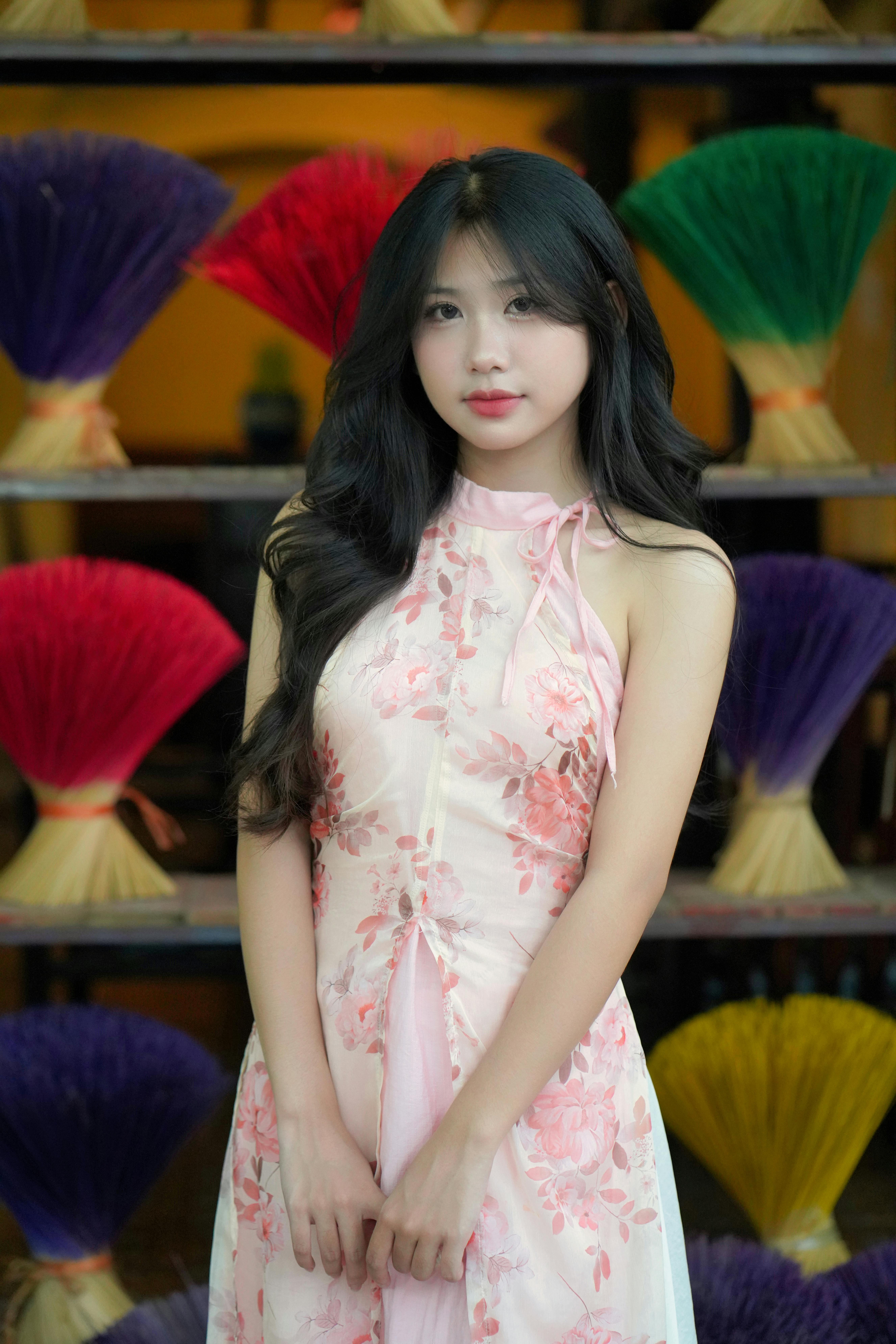 Young woman in floral dress posing with vibrant incense sticks in background.