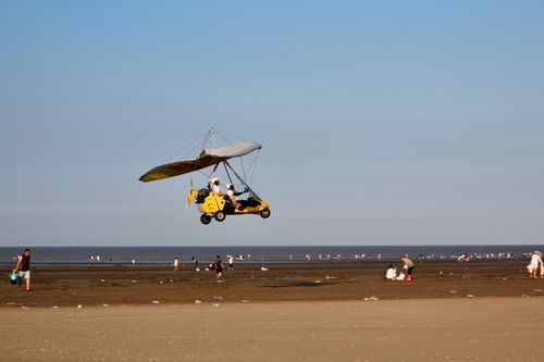 Free An ultralight aircraft soars above a crowded beach on a sunny day, capturing adventure and leisure. Stock Photo