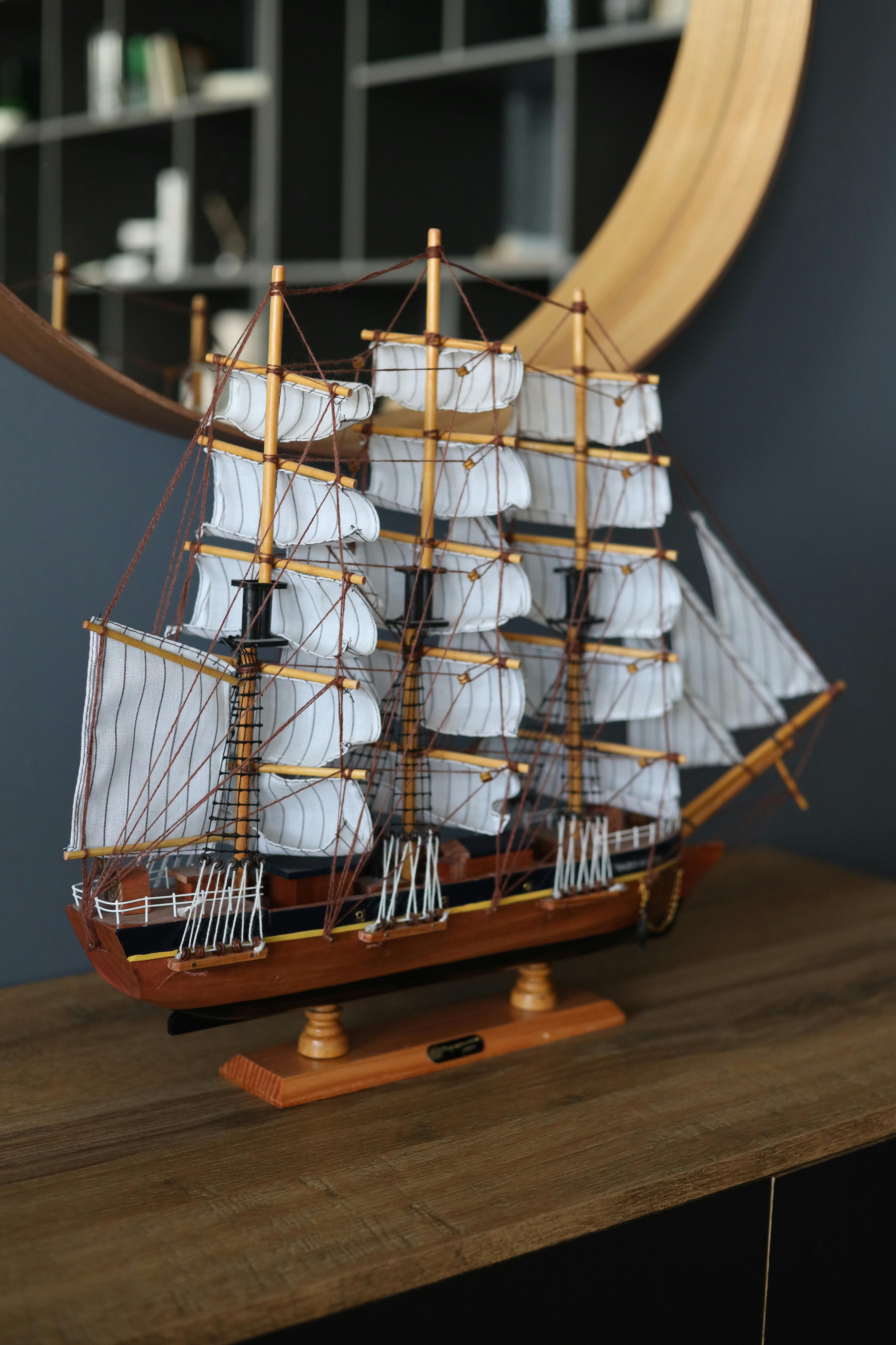 Free Elegant model ship with white sails showcased on a wooden shelf indoors. Stock Photo