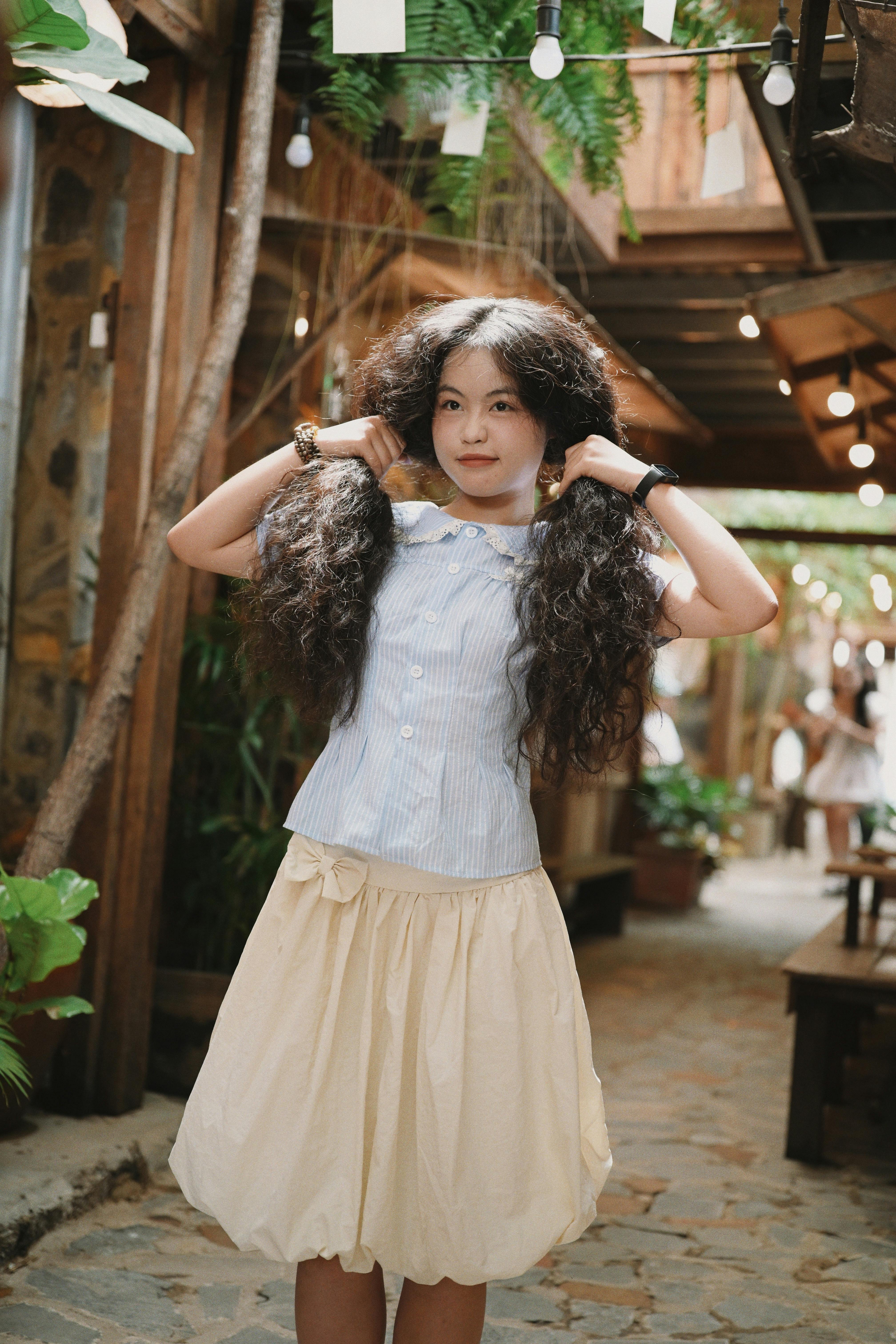 A young girl showcasing her long curly hair in a charming rustic setting with string lights.