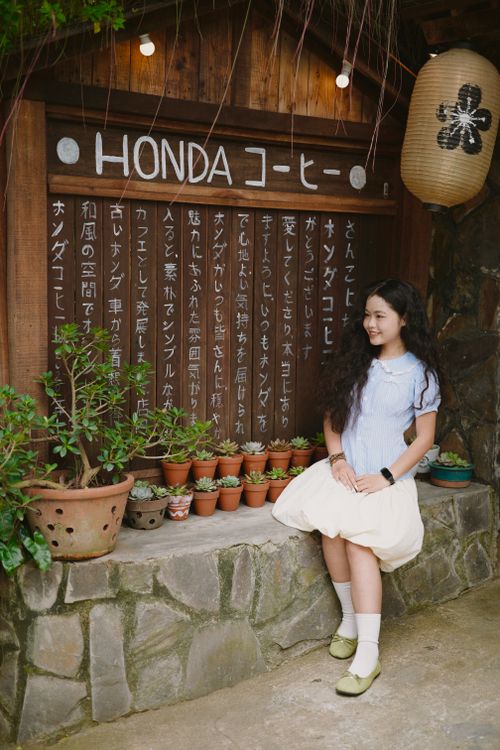 Free Girl sitting by a Japanese signboard with potted plants at a coffee shop. Stock Photo