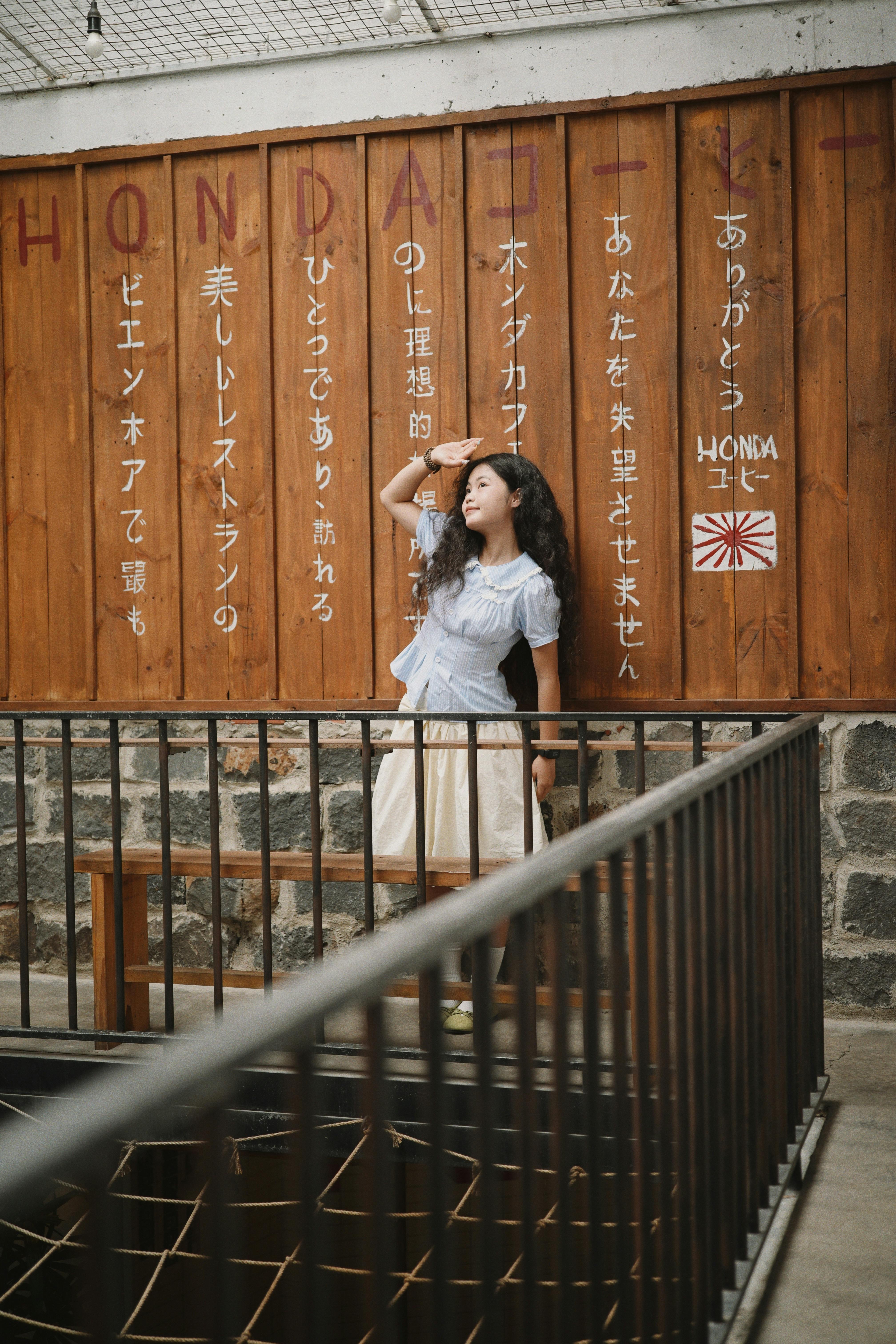 Young woman poses against Japanese text wall in a stylish cafe.