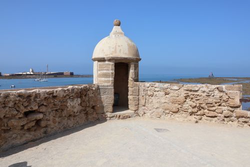 Free A historic stone watchtower overlooking the serene coastline of Cádiz, Spain, under a clear blue sky. Stock Photo