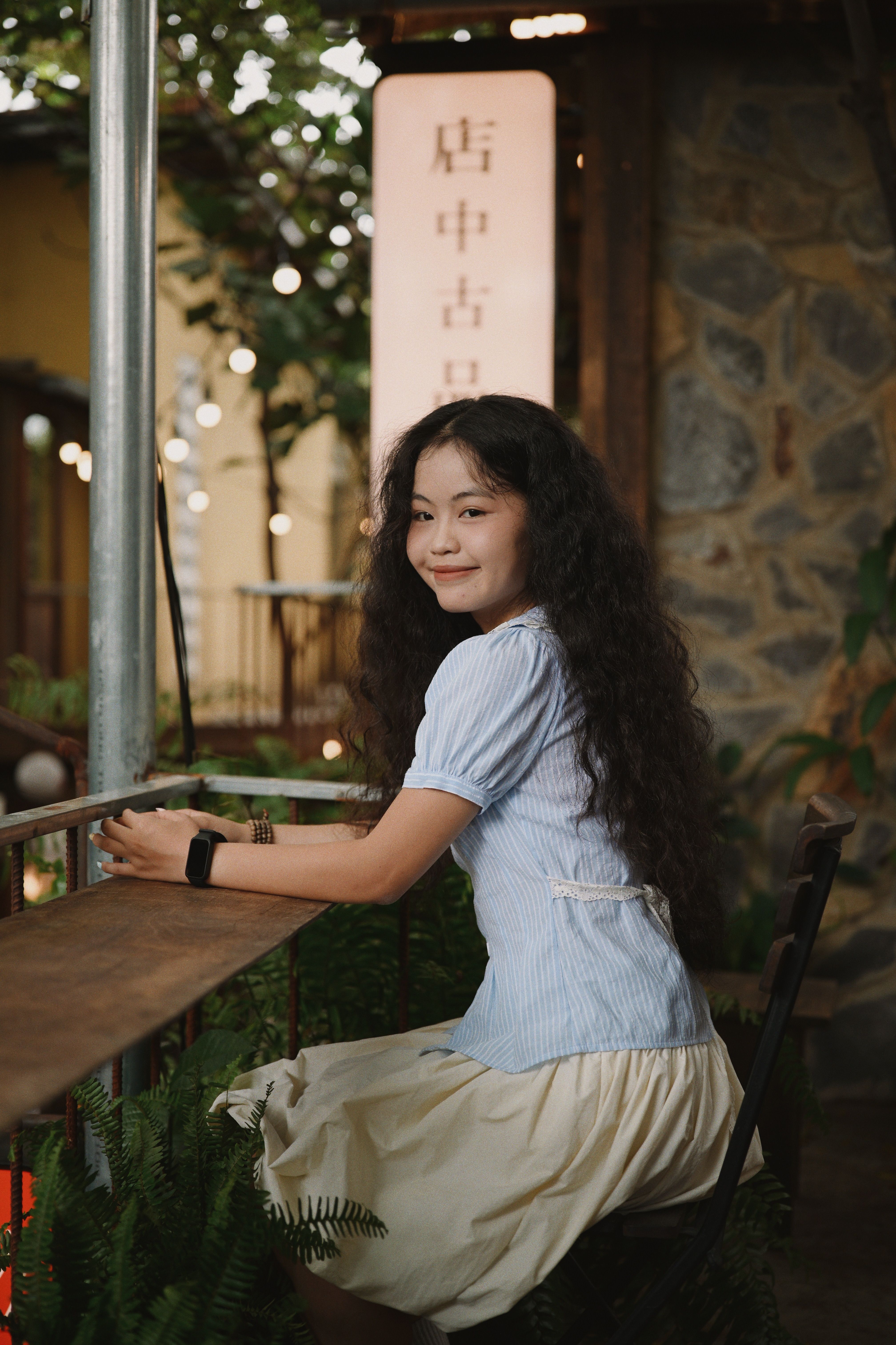 Smiling young woman sitting outdoors in cozy cafe setting.