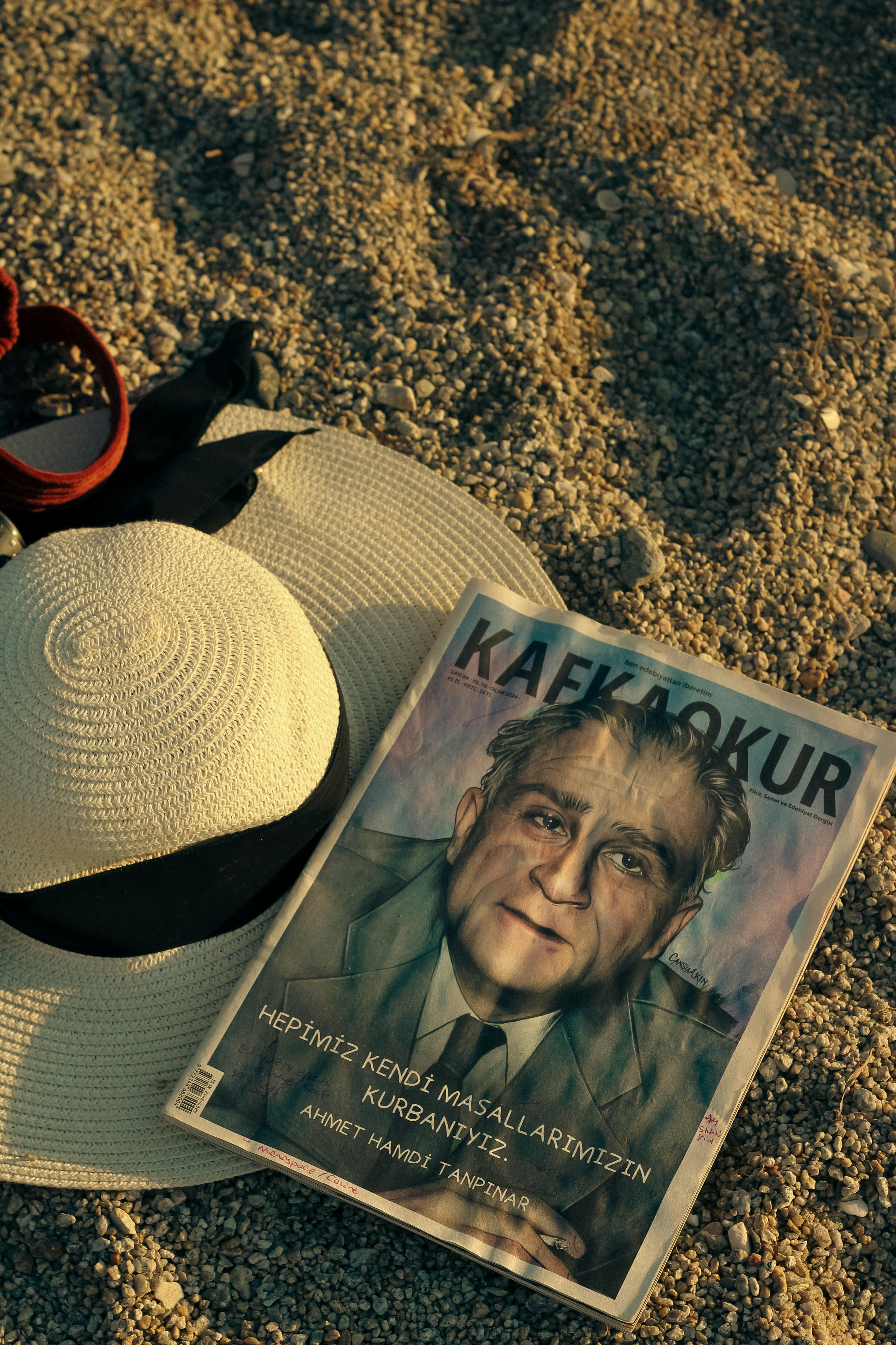 A summer beach scene featuring a magazine and straw hat on pebbles.