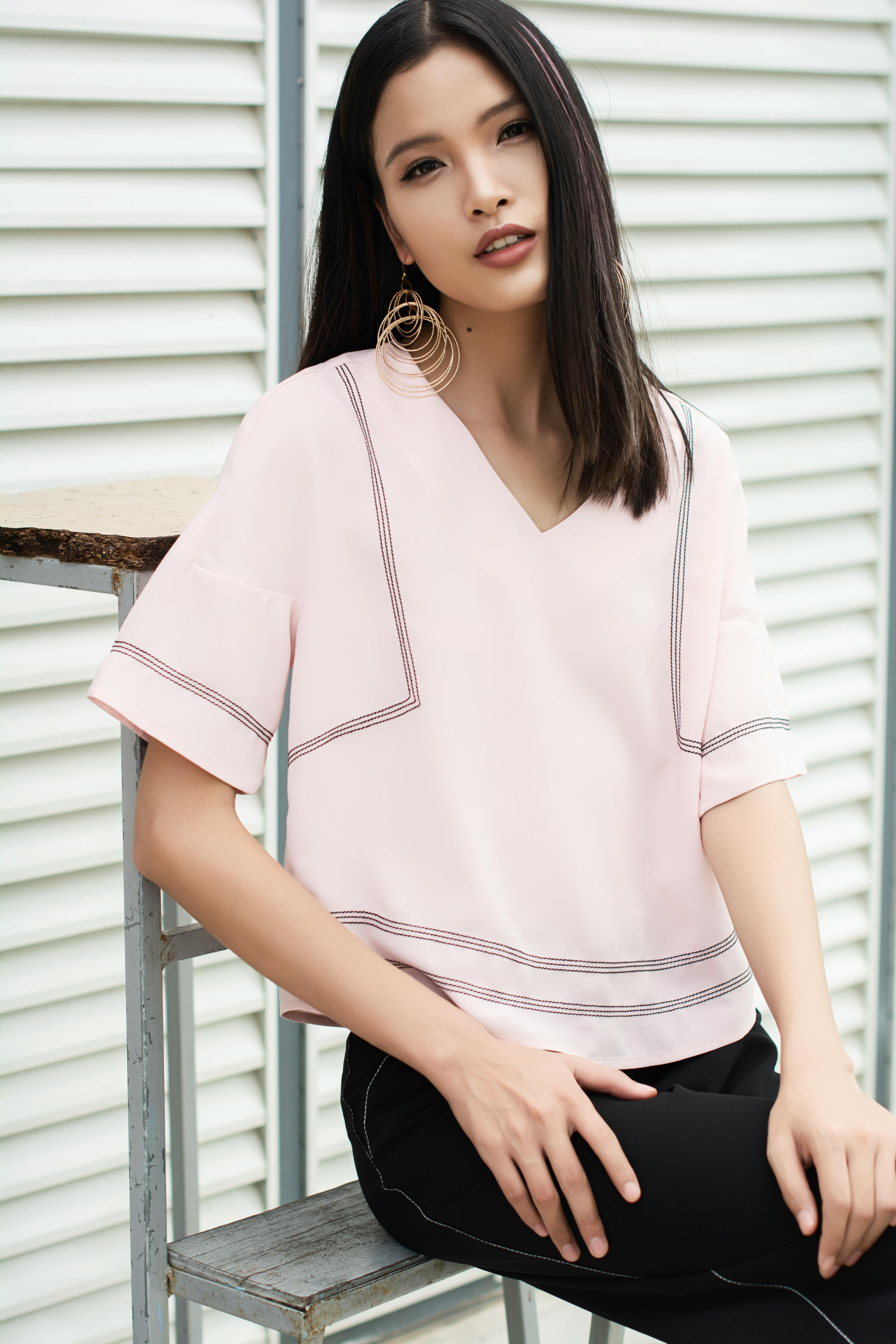 Kostnadsfria Porträtt av en trendig asiatisk kvinna i rosa blus och iögonfallande örhängen som sitter utomhus. Stock foto