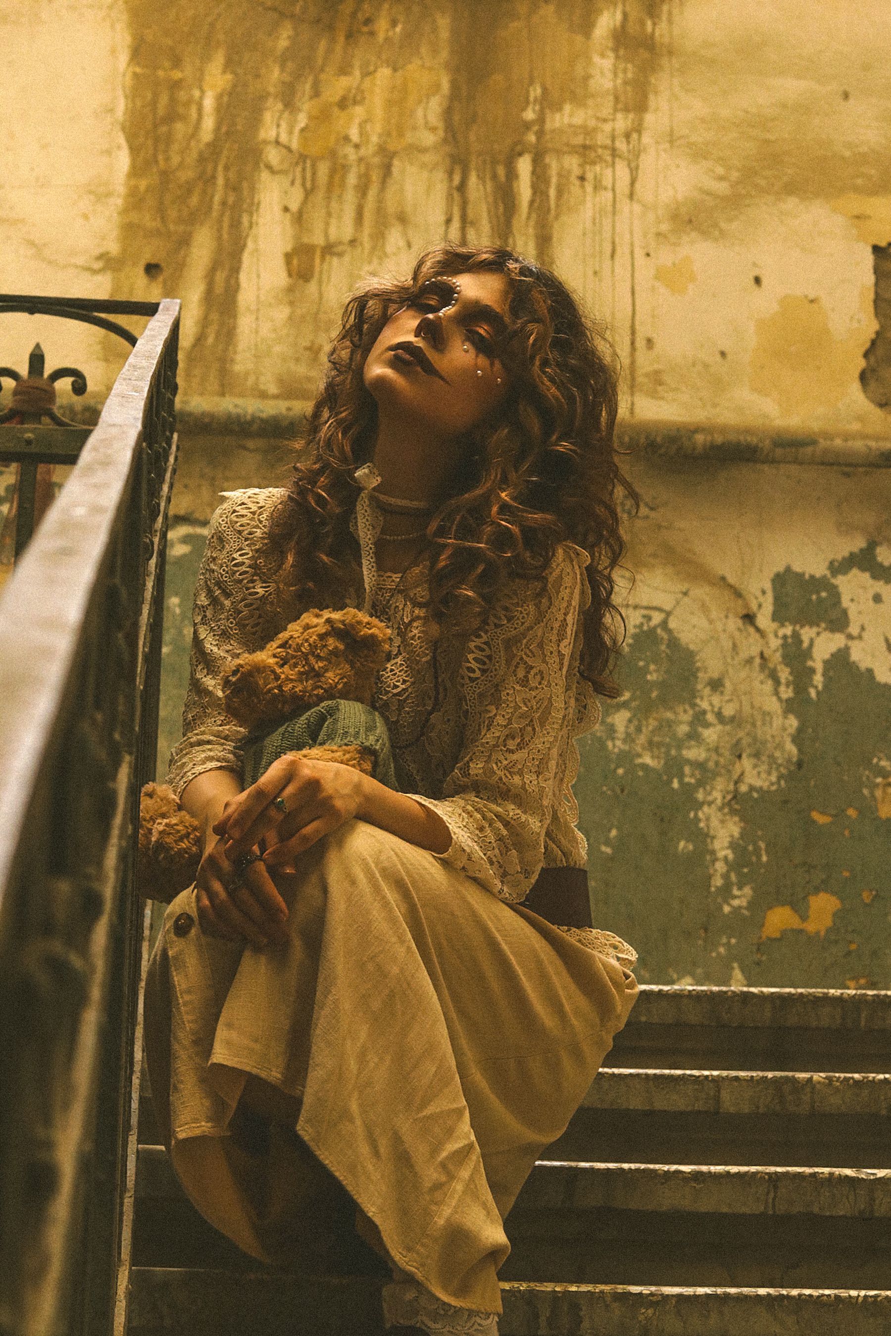 A woman in vintage attire sits on stairs, exuding a moody atmosphere.