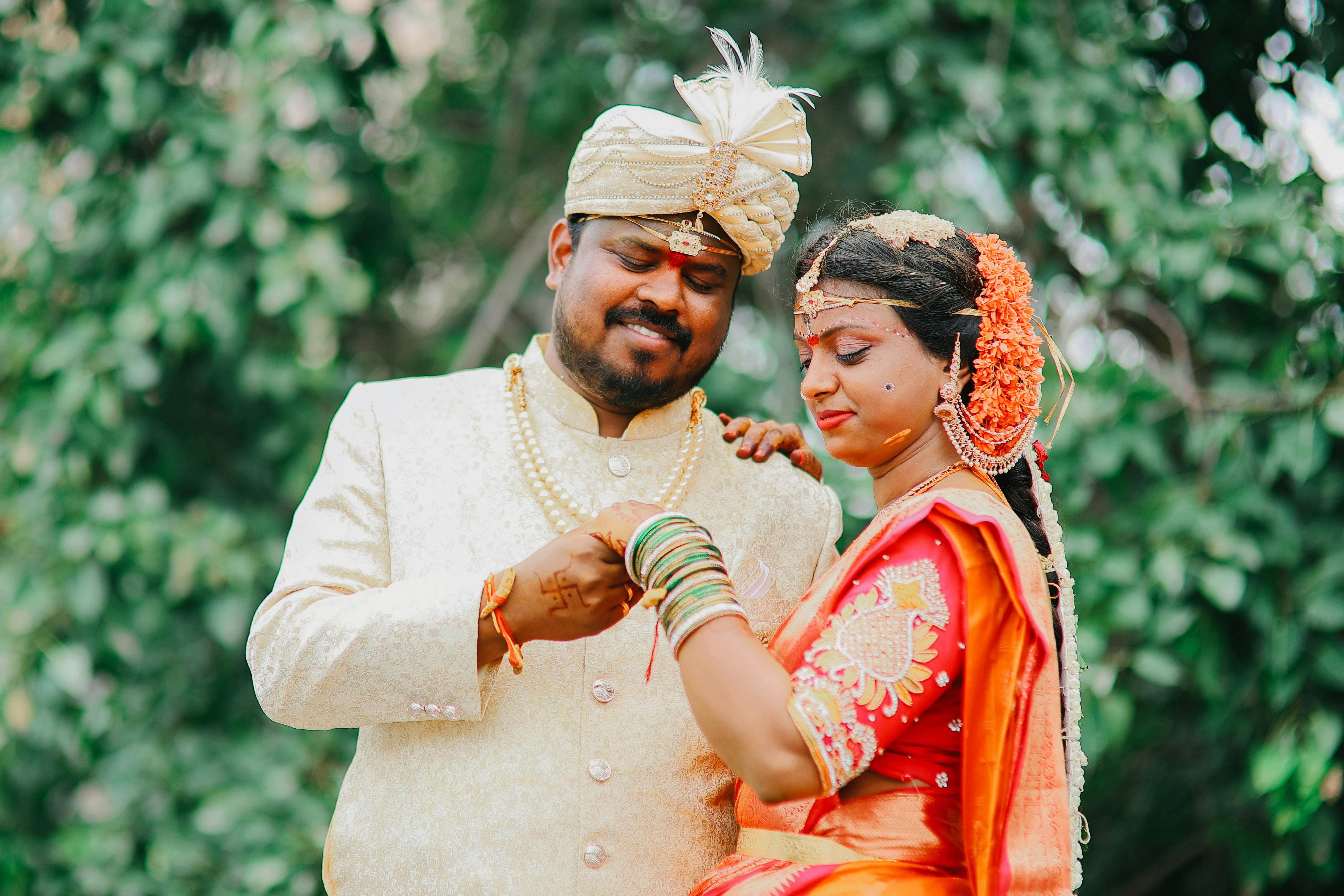 A joyful South Indian couple celebrates their wedding day in Telangana, adorned in traditional attire against a lush backdrop.