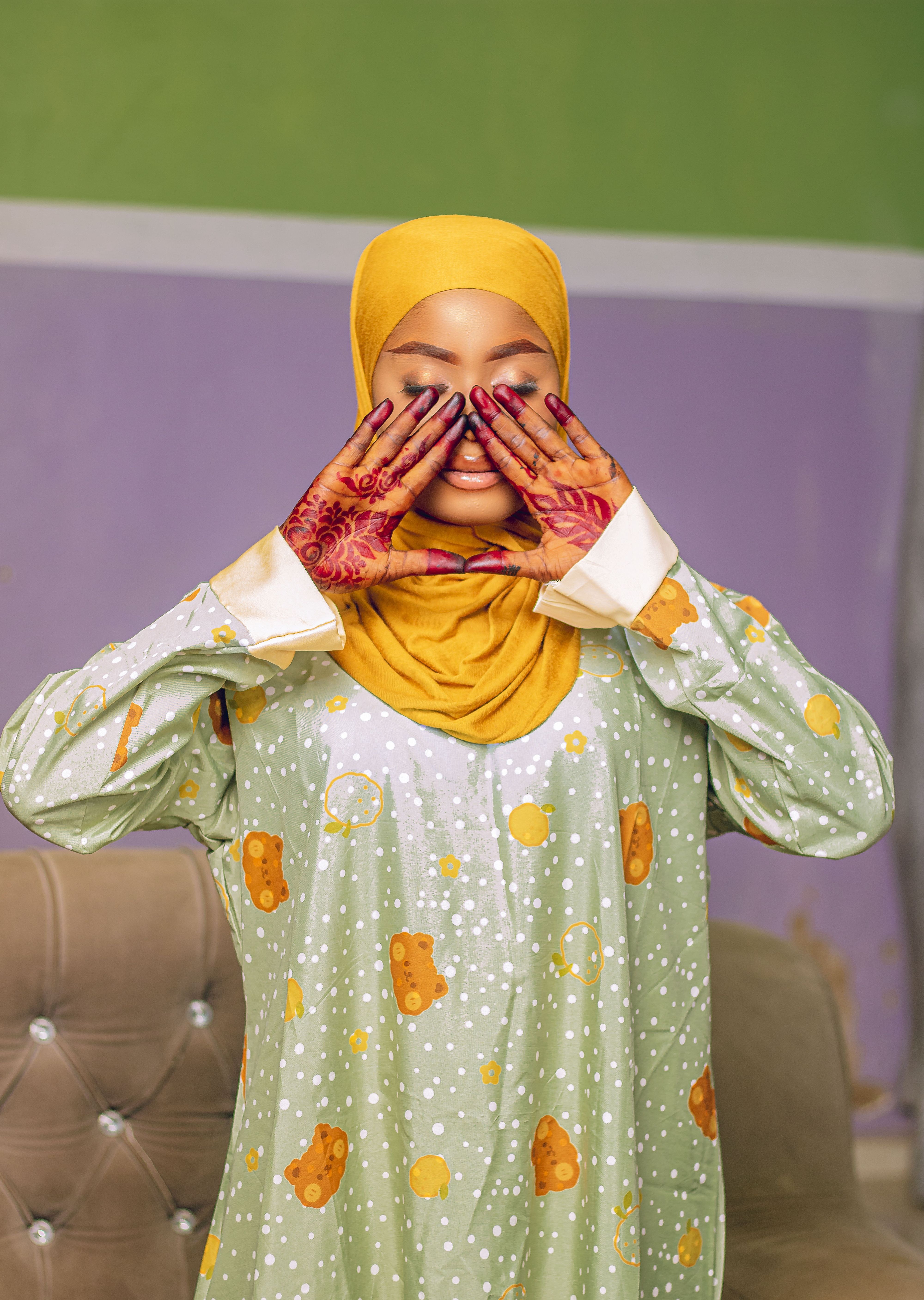 A woman wearing a hijab and pajamas with floral henna on her hands, posing indoors.