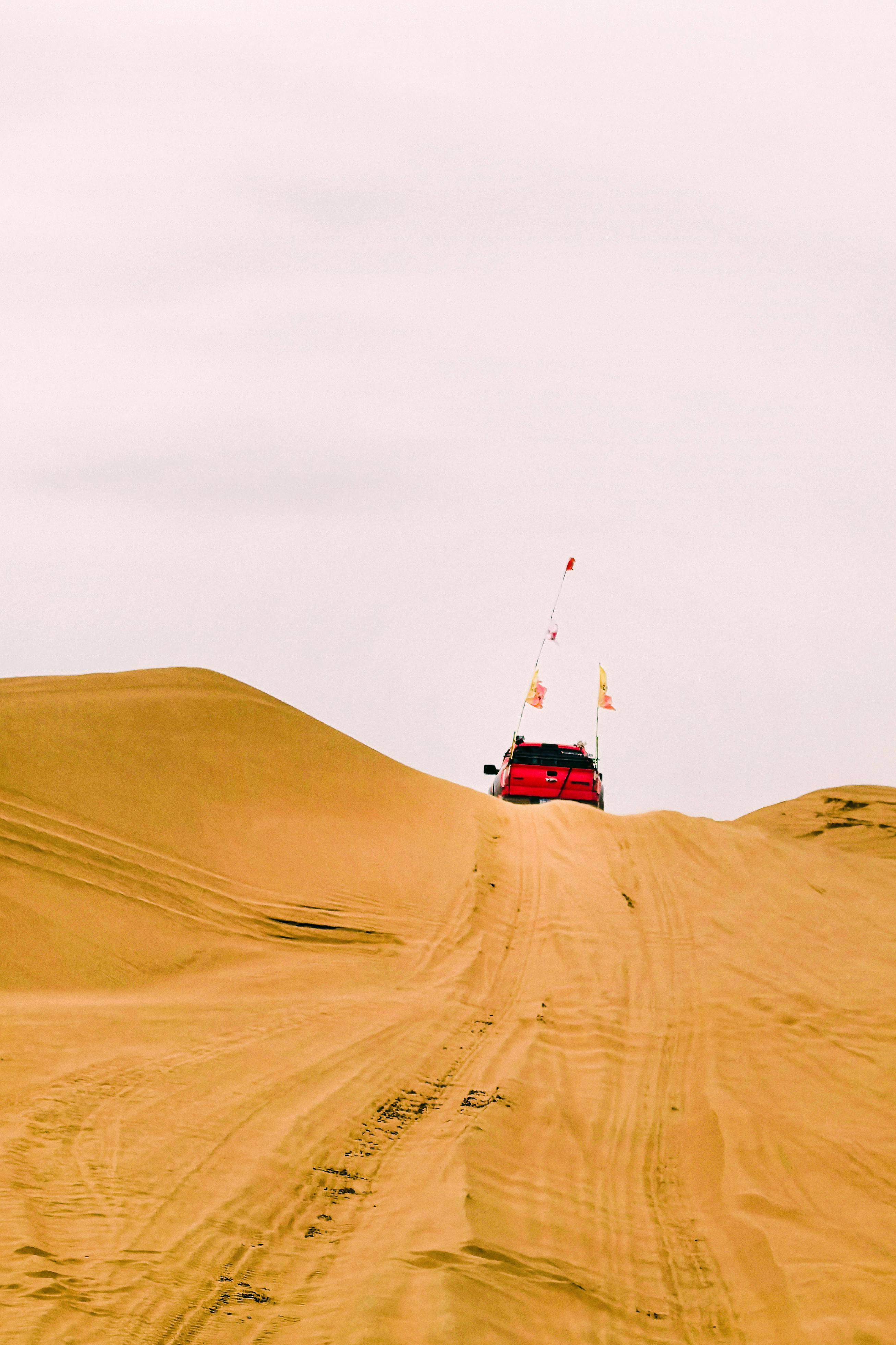A red SUV ascends sandy desert dunes, capturing adventure and exploration.