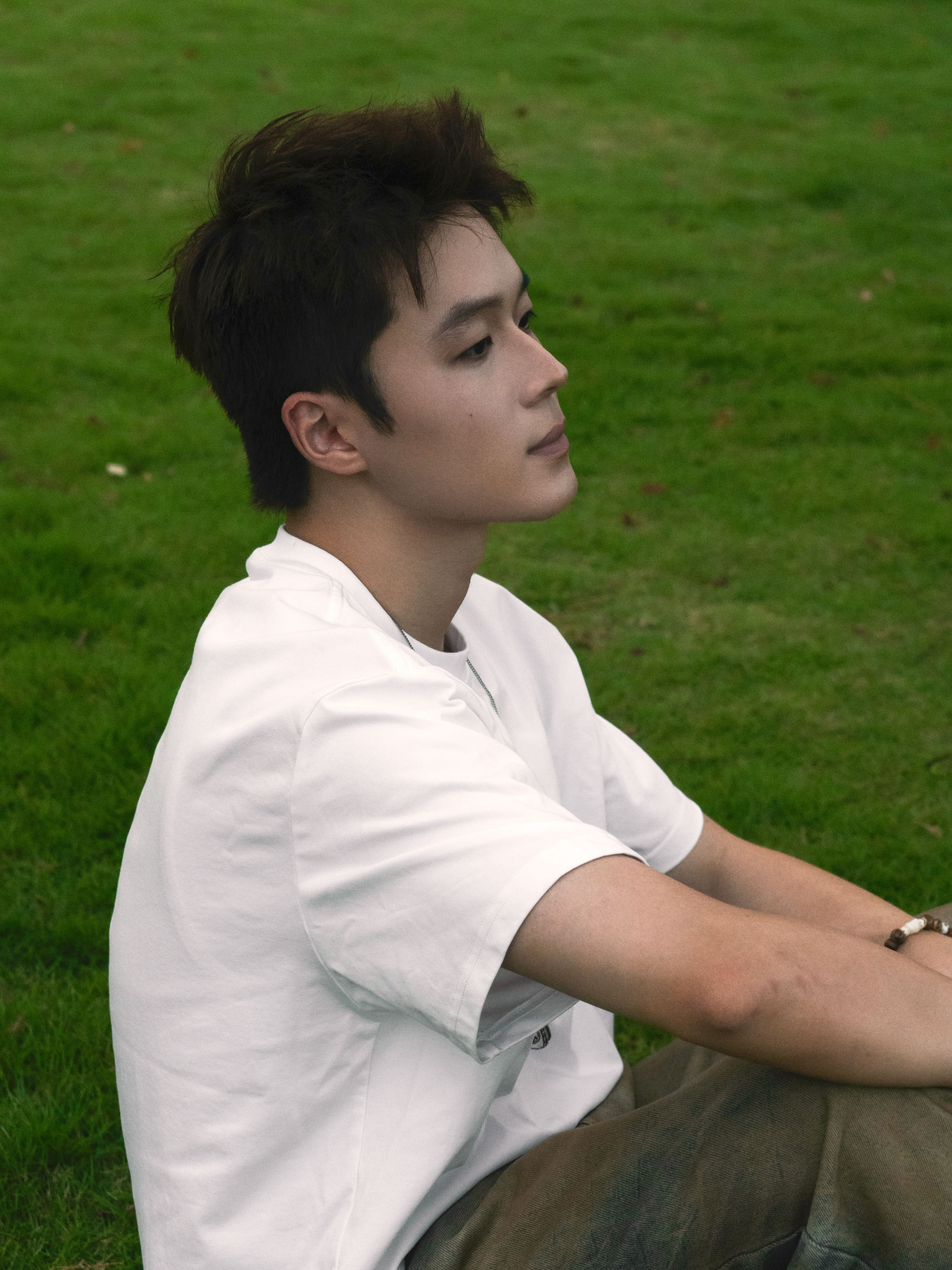 Portrait of a young man sitting on the grass, enjoying a calm moment in a park.