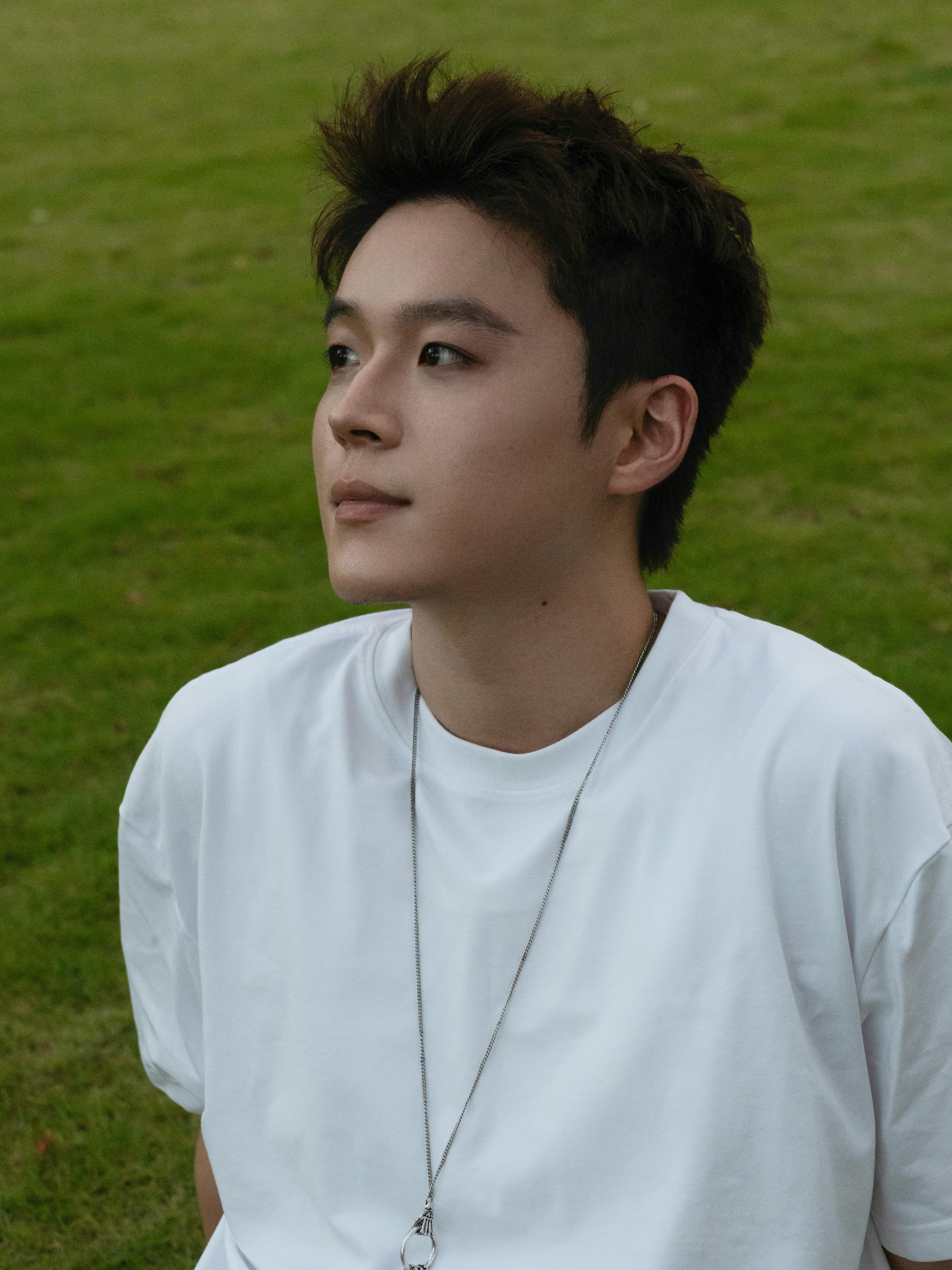 Portrait of a young man sitting outdoors in a park with green grass.