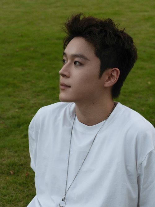 Free Profile of a young man sitting on grass, looking thoughtful. Stock Photo