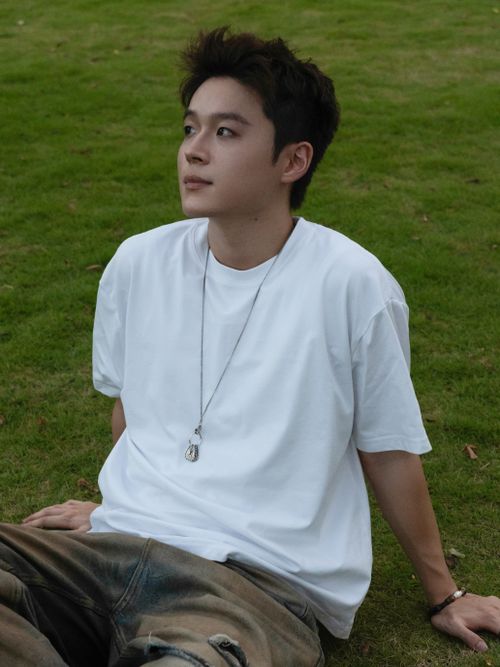 Free A young man in casual attire sitting relaxed on a grassy lawn, enjoying an outdoor moment. Stock Photo