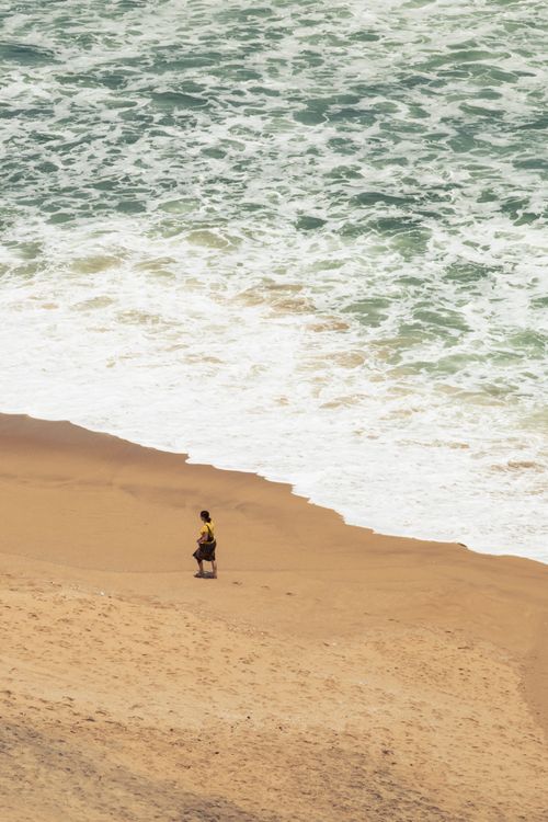 Free A lone person walks on a sandy beach with waves crashing, evoking calm and solitude. Stock Photo