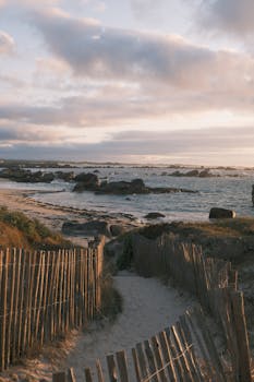 Scenic coastal pathway leading to ocean with dramatic sunset sky and rugged rocks.