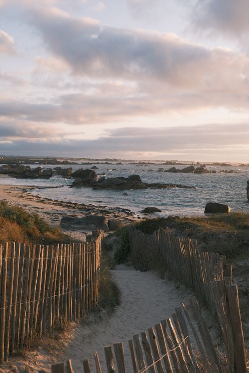 Free Scenic coastal pathway leading to ocean with dramatic sunset sky and rugged rocks. Stock Photo