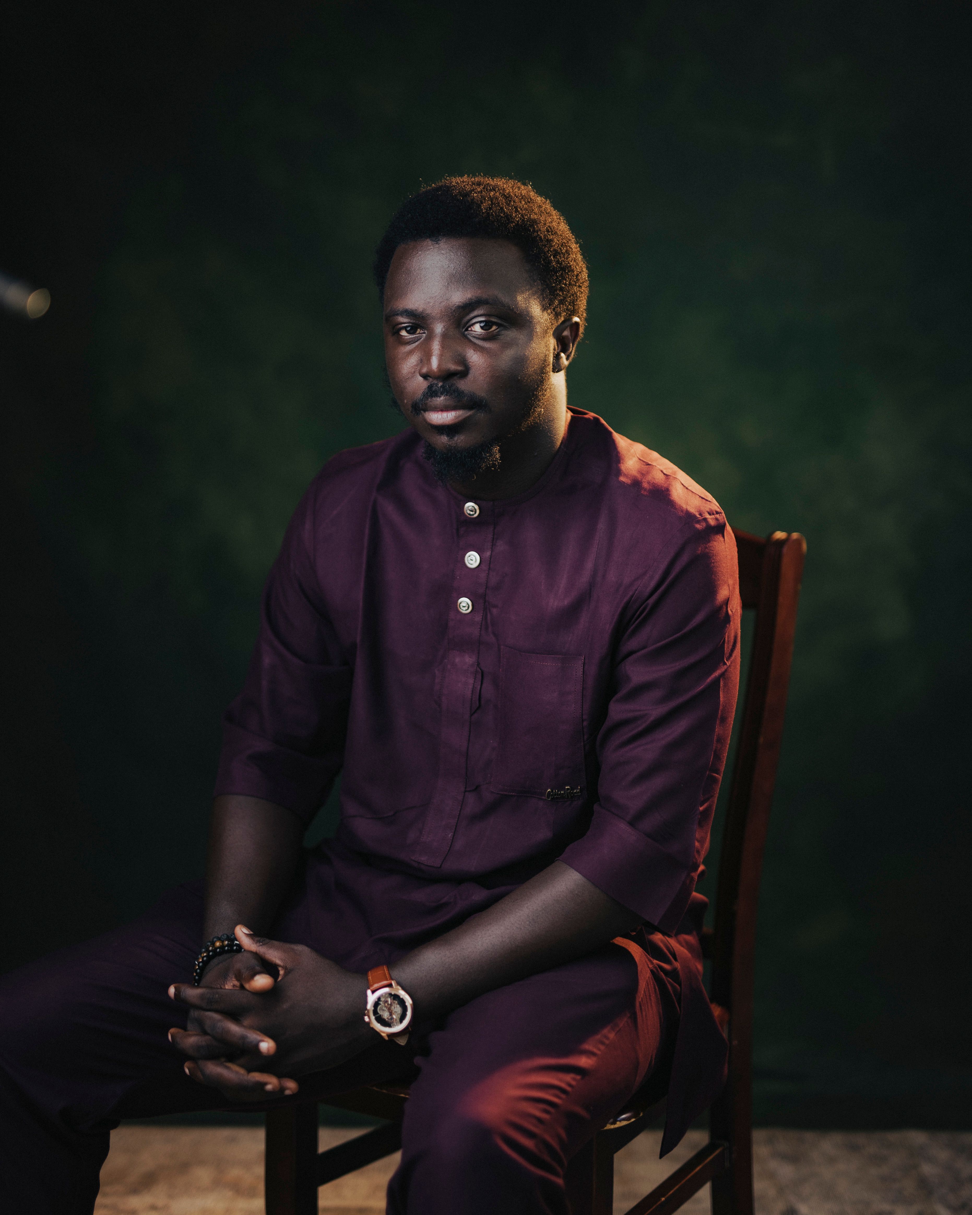 Studio portrait of a man in traditional African attire, seated calmly.