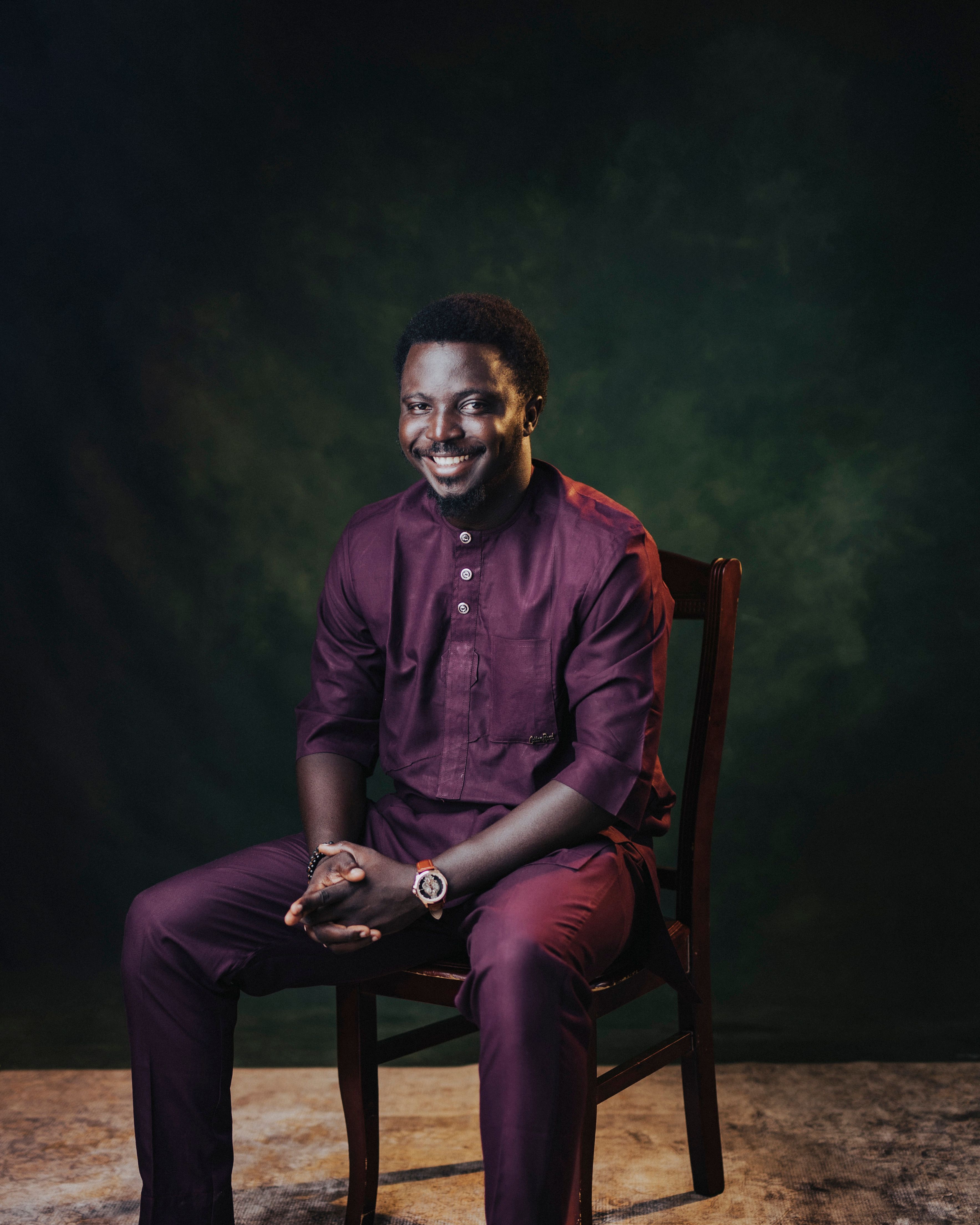 Smiling man seated in traditional African clothes against a textured backdrop.