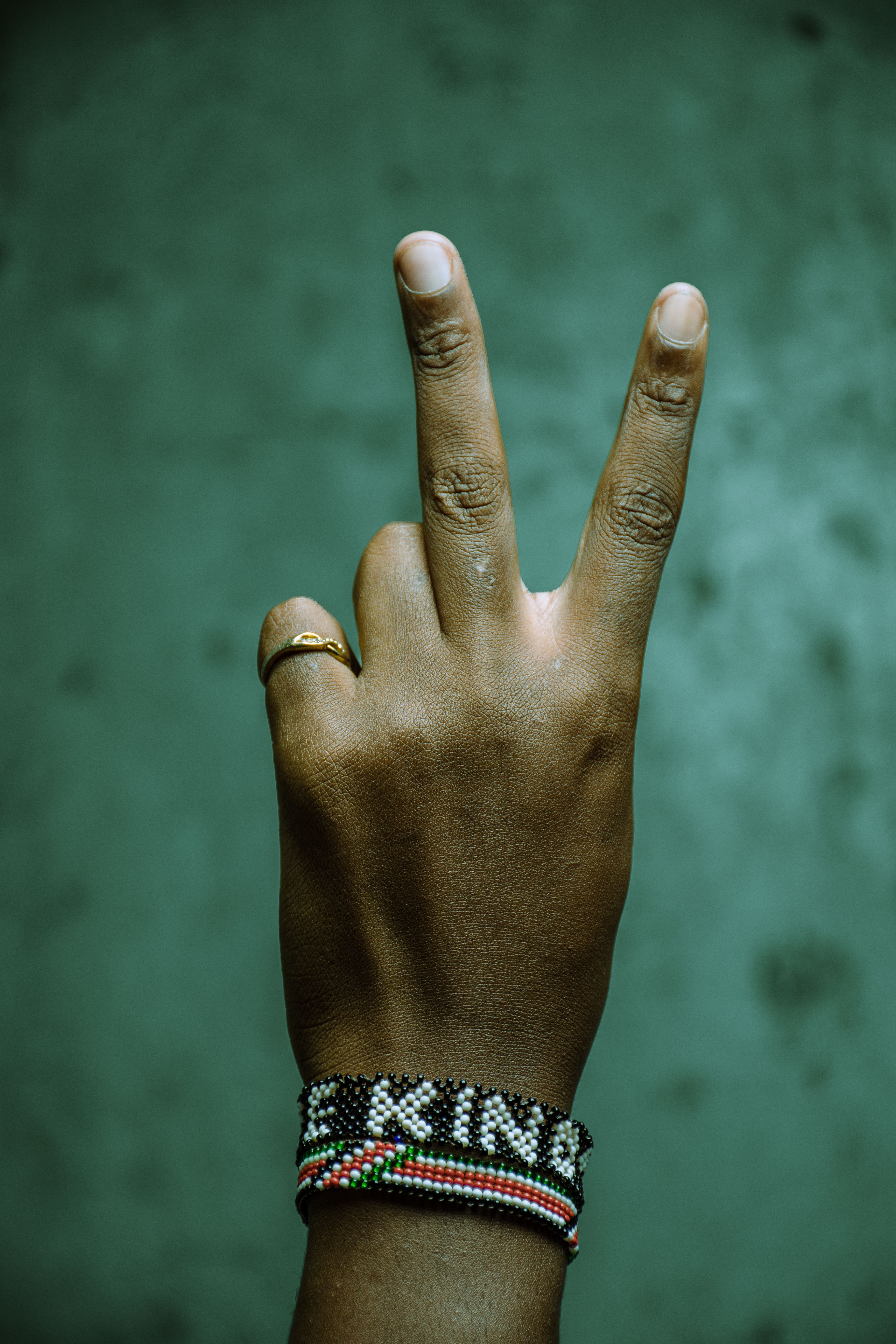 A hand showing a peace sign adorned with a colorful Kenyan wristband symbolizing tranquility.