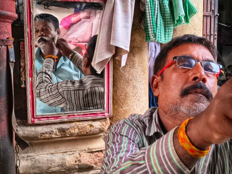 Barber shaves a client's beard in a vibrant street setting, captured uniquely with reflection.