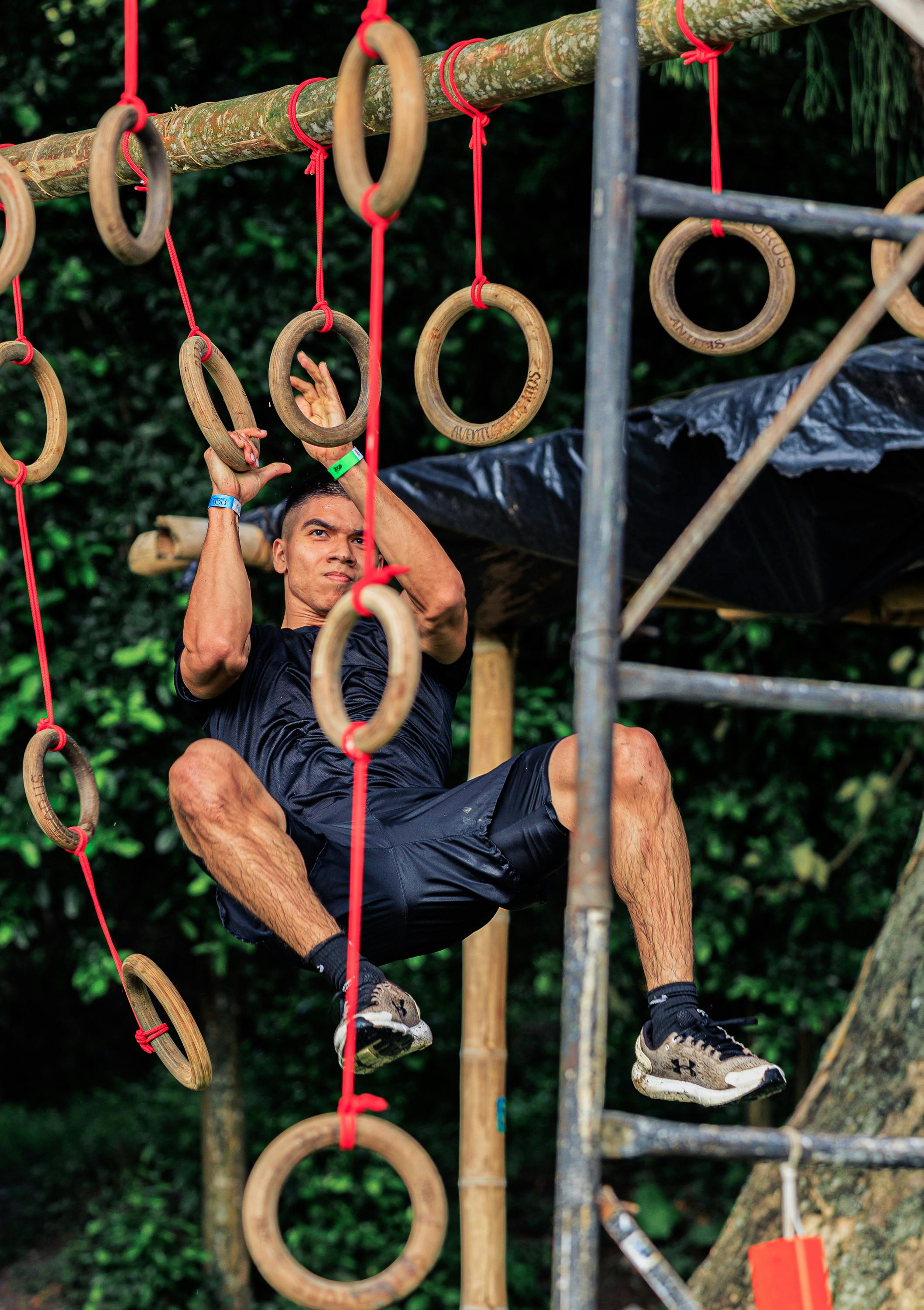 Focused man tackling outdoor obstacle course with wooden rings in action.