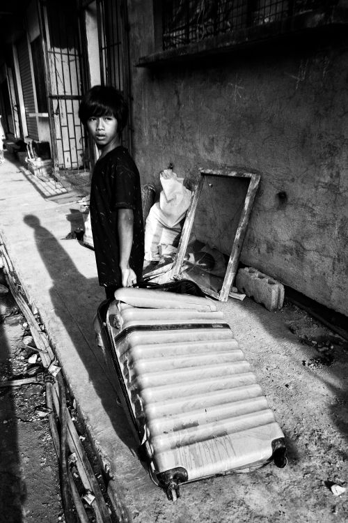 Free Black and white photo of a young person with a suitcase in an urban alleyway. Stock Photo
