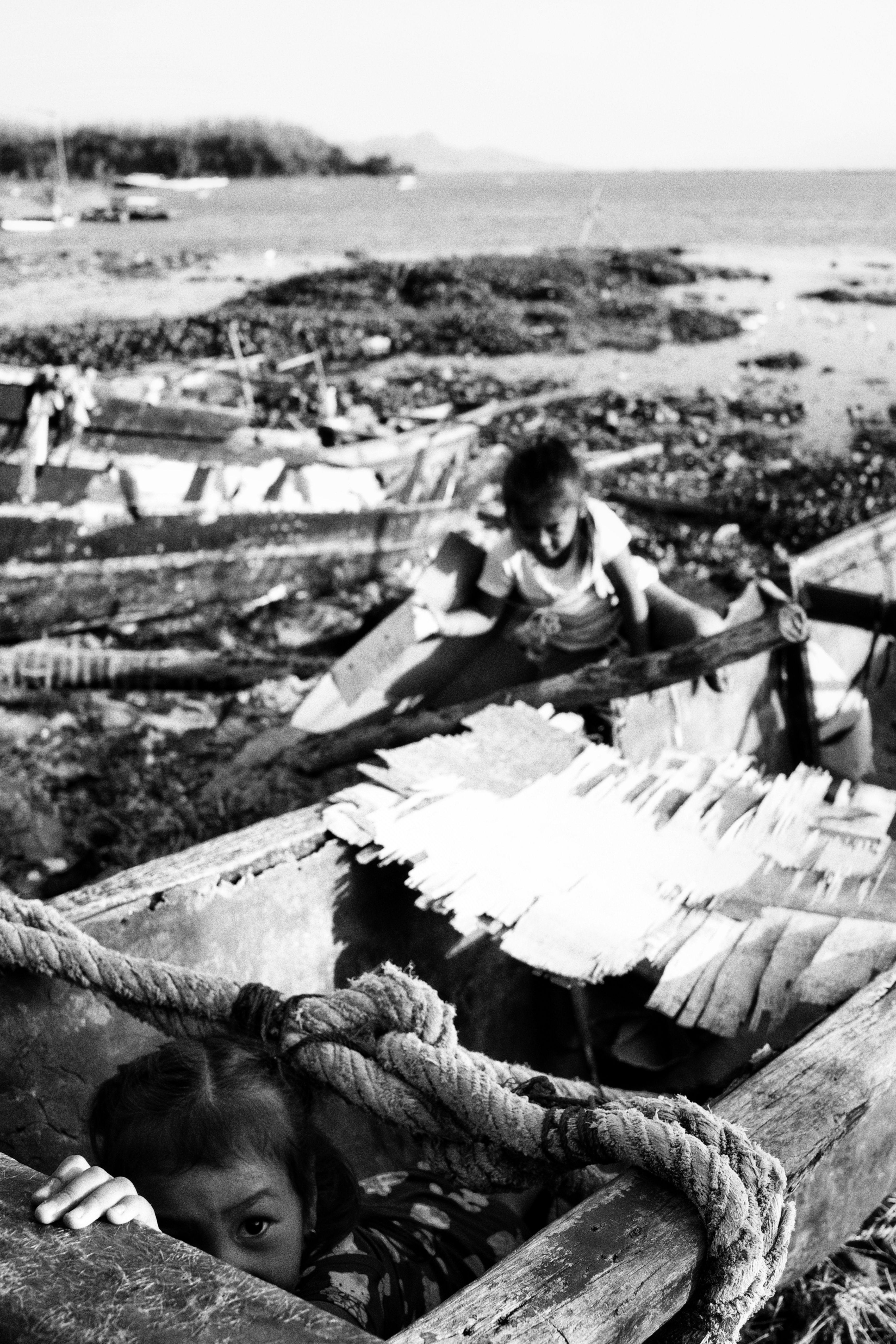 Children play in old boats by a rocky seaside, creating a nostalgic scene.