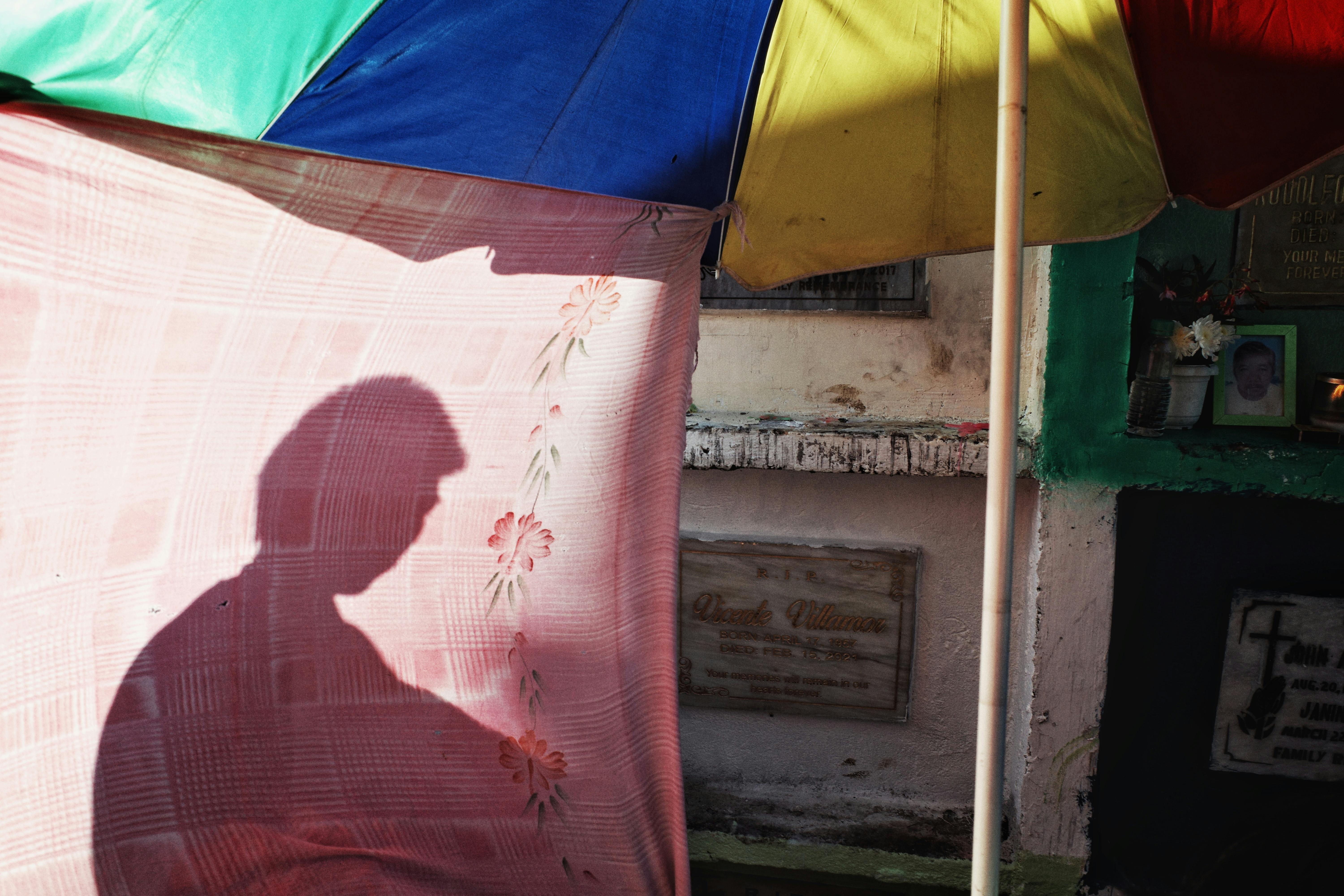 Silhouette under a vivid umbrella at a market, casting shadows on a floral sheet.