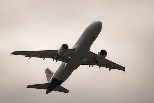 Airplane viewed from below, taking off from Munich Airport under cloudy skies.