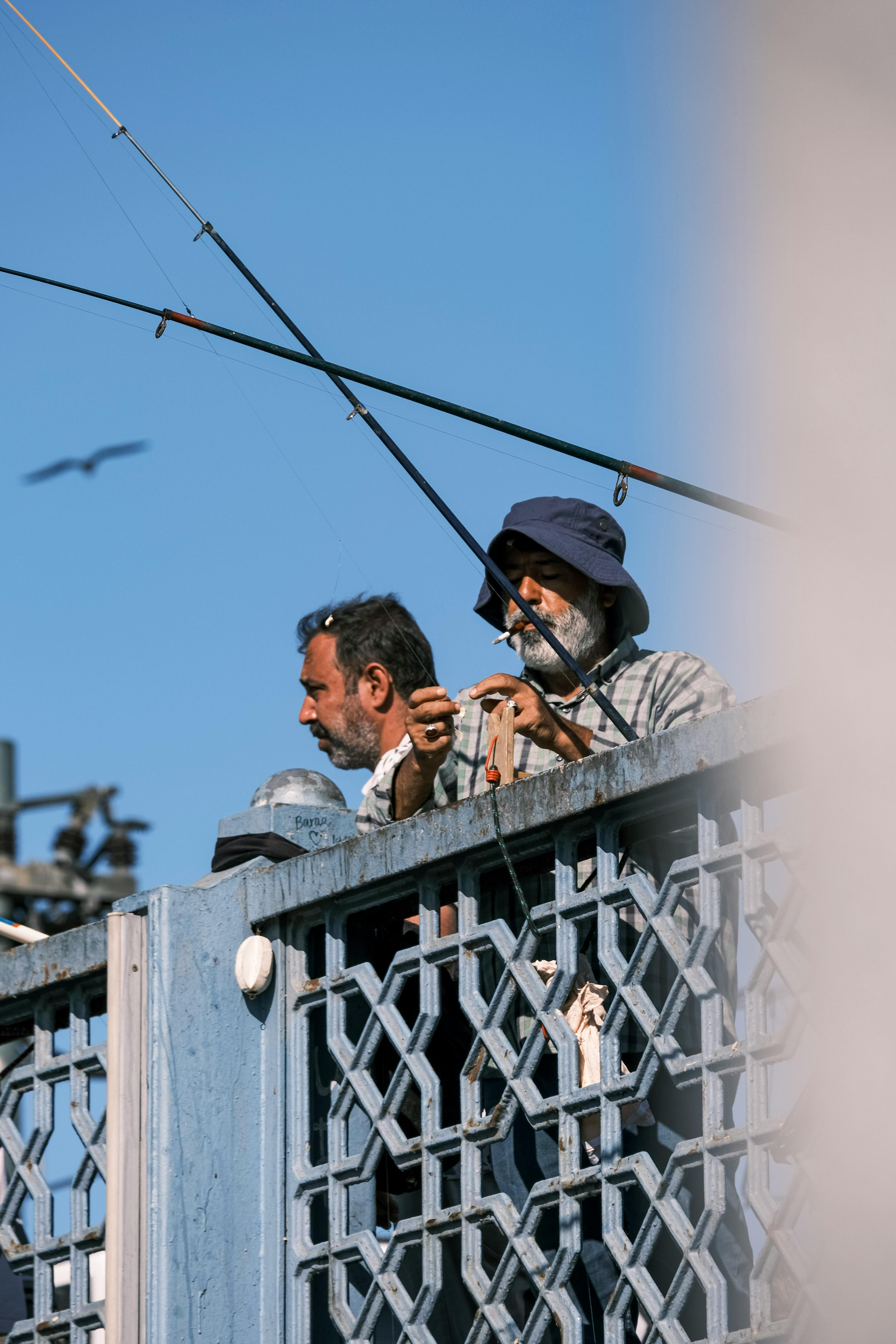 Two men fishing from a bridge under a clear blue sky, showcasing leisure and outdoor activity.