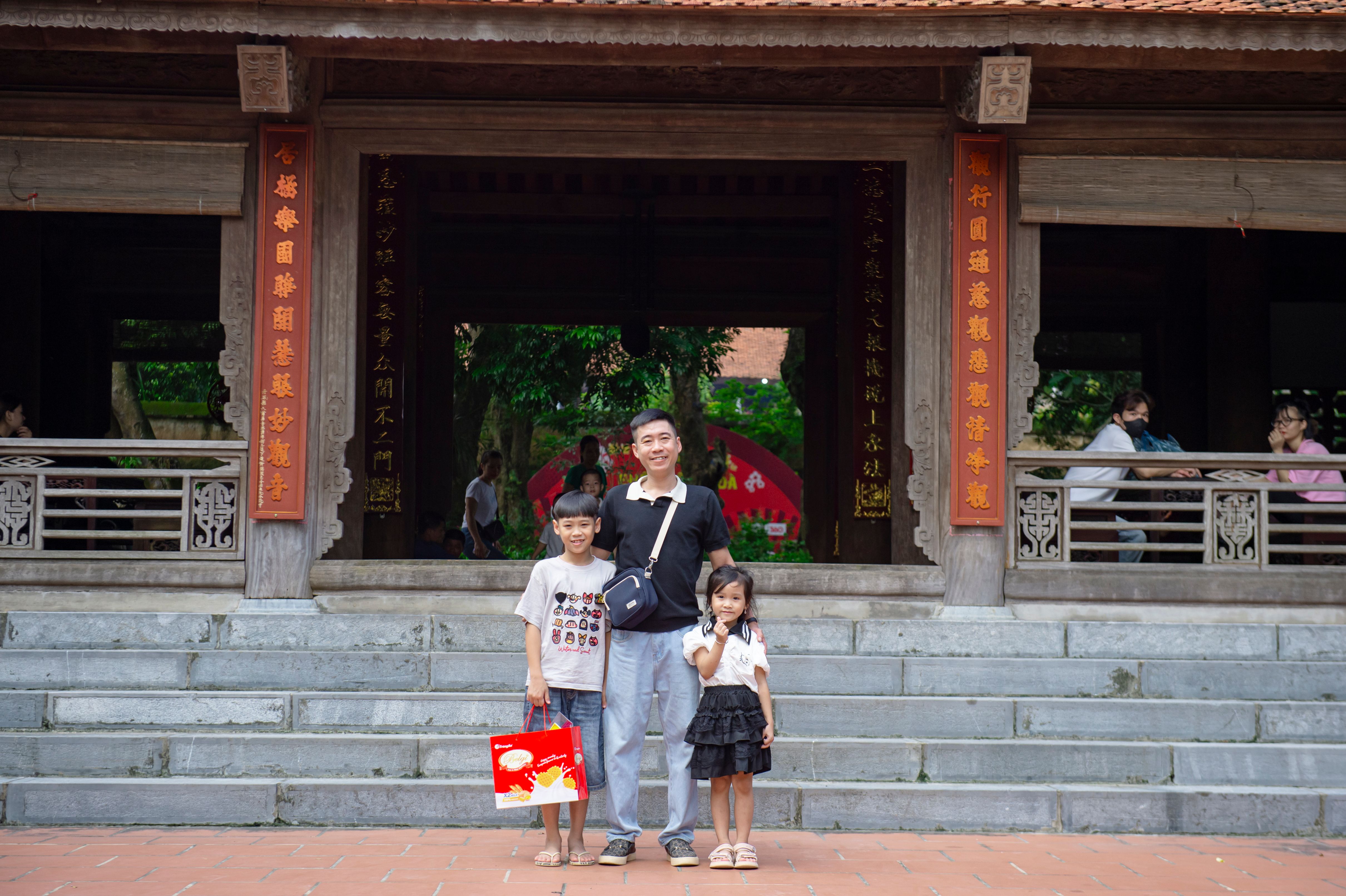 A family poses at a historical site in Hà Nội, Vietnam, showcasing traditional architecture.