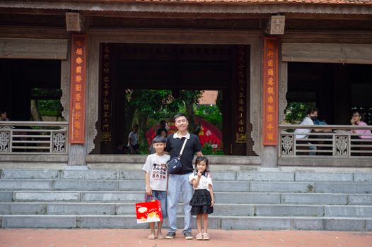 A family poses at a historical site in Hà Nội, Vietnam, showcasing traditional architecture.