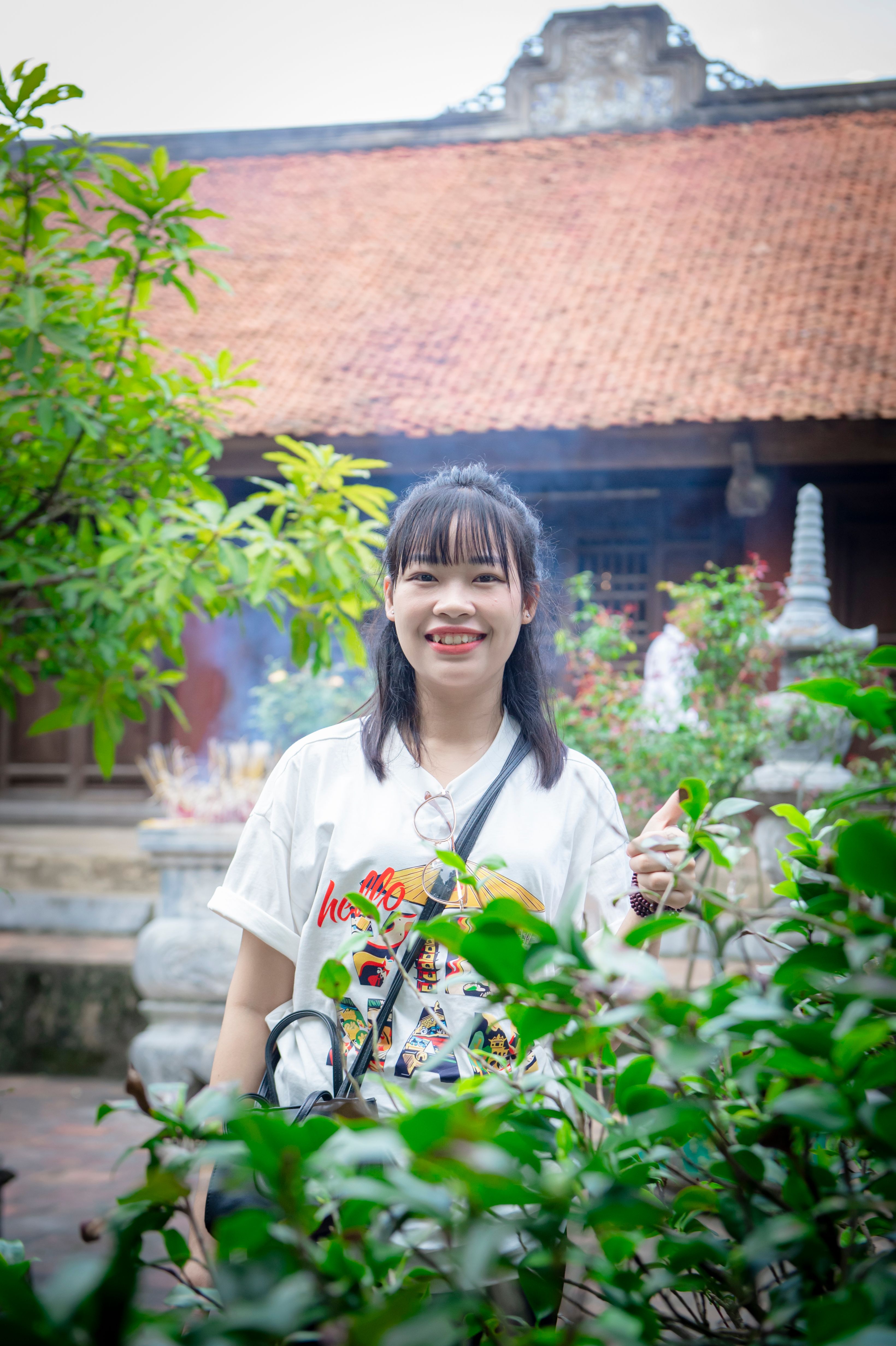 Young woman smiling in front of traditional Vietnamese temple garden.
