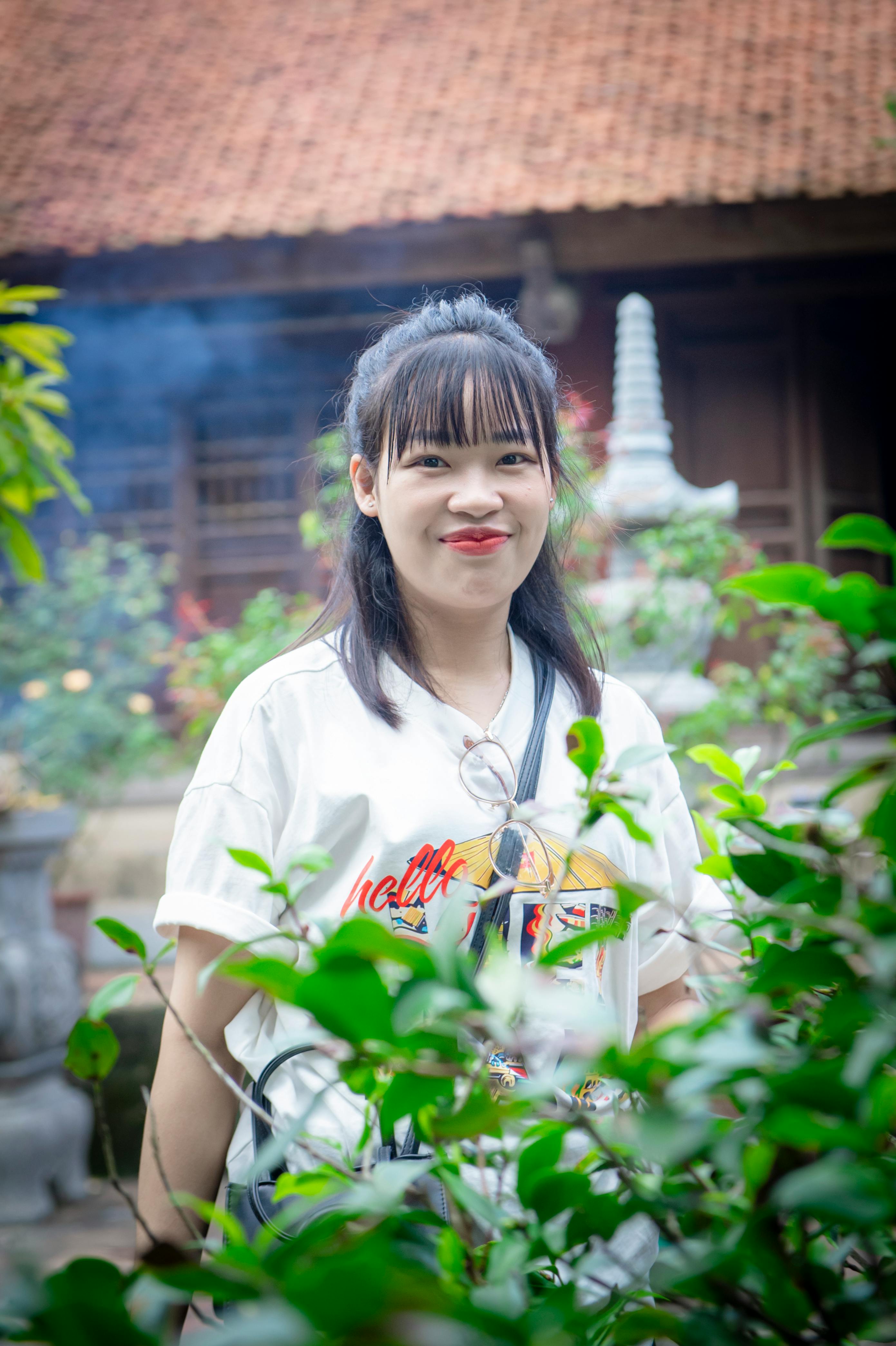 Young woman smiling in a lush temple garden in Hà Nội, Việt Nam.