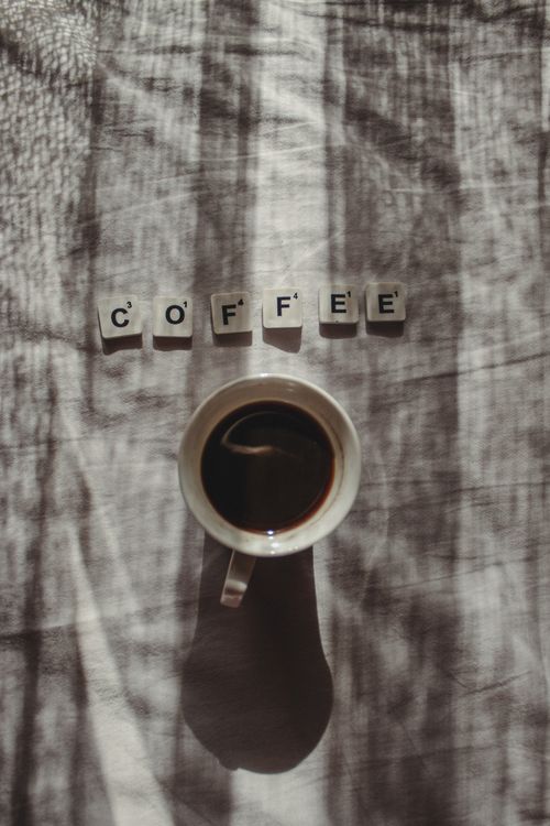 Free A top view of a coffee cup with scrabble tiles spelling 'coffee' and artistic shadows. Stock Photo