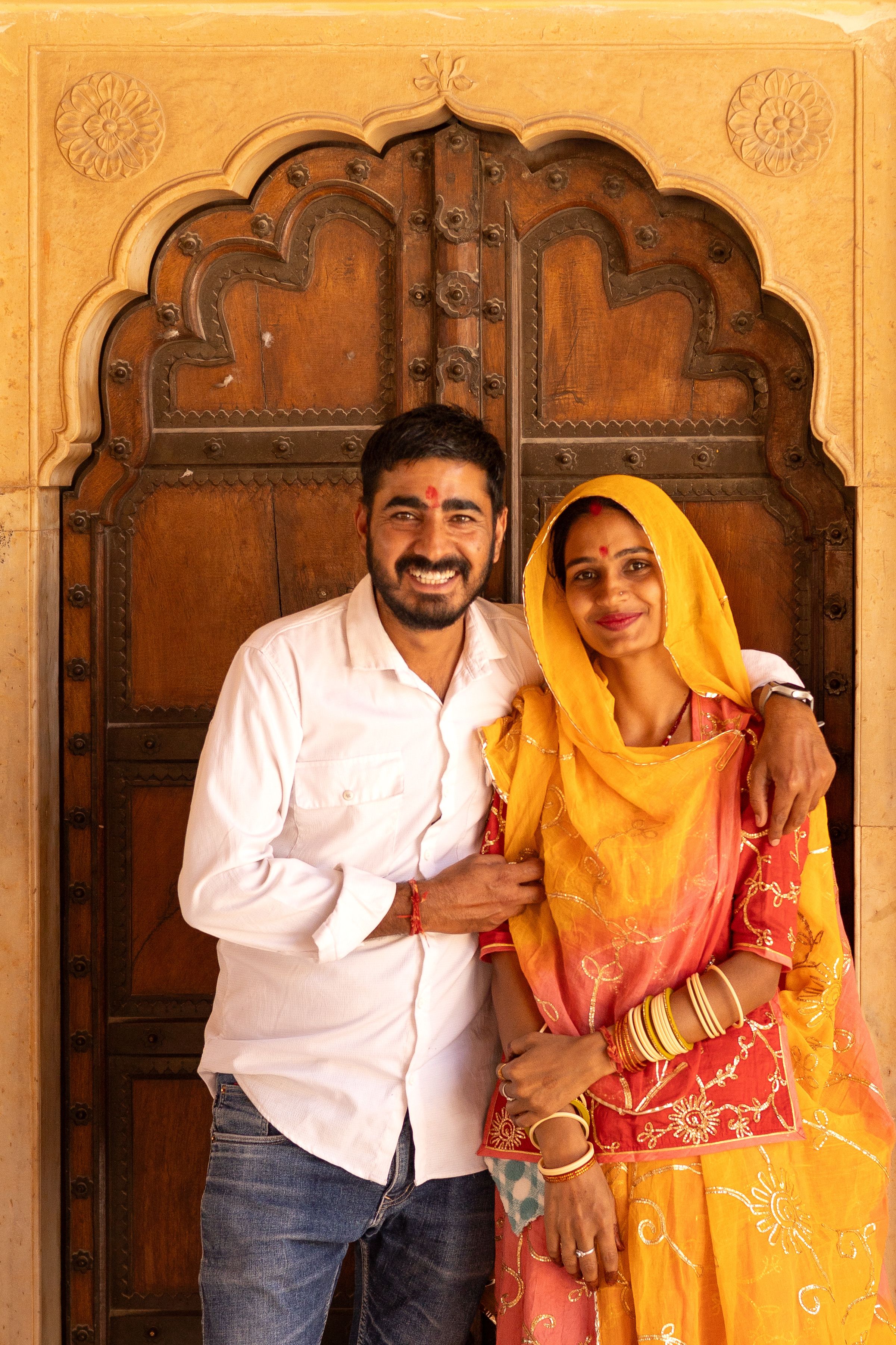 Happy couple in traditional attire posing in front of a carved door in Jaipur.